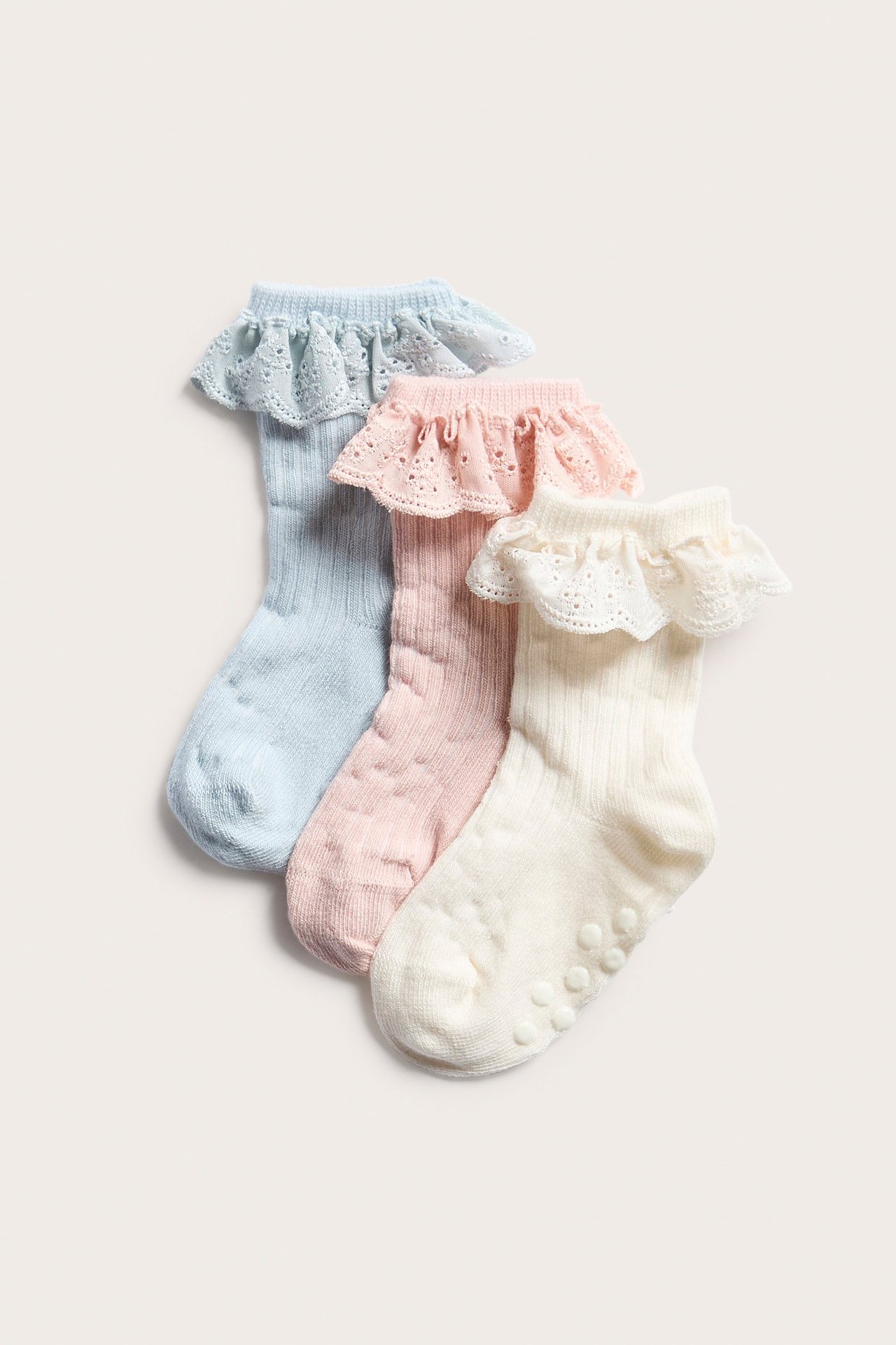 Nærbilde: Tre ribbestrikkede babysokker i lys rosa, lys blå og offwhite, alle med blondekanter.
