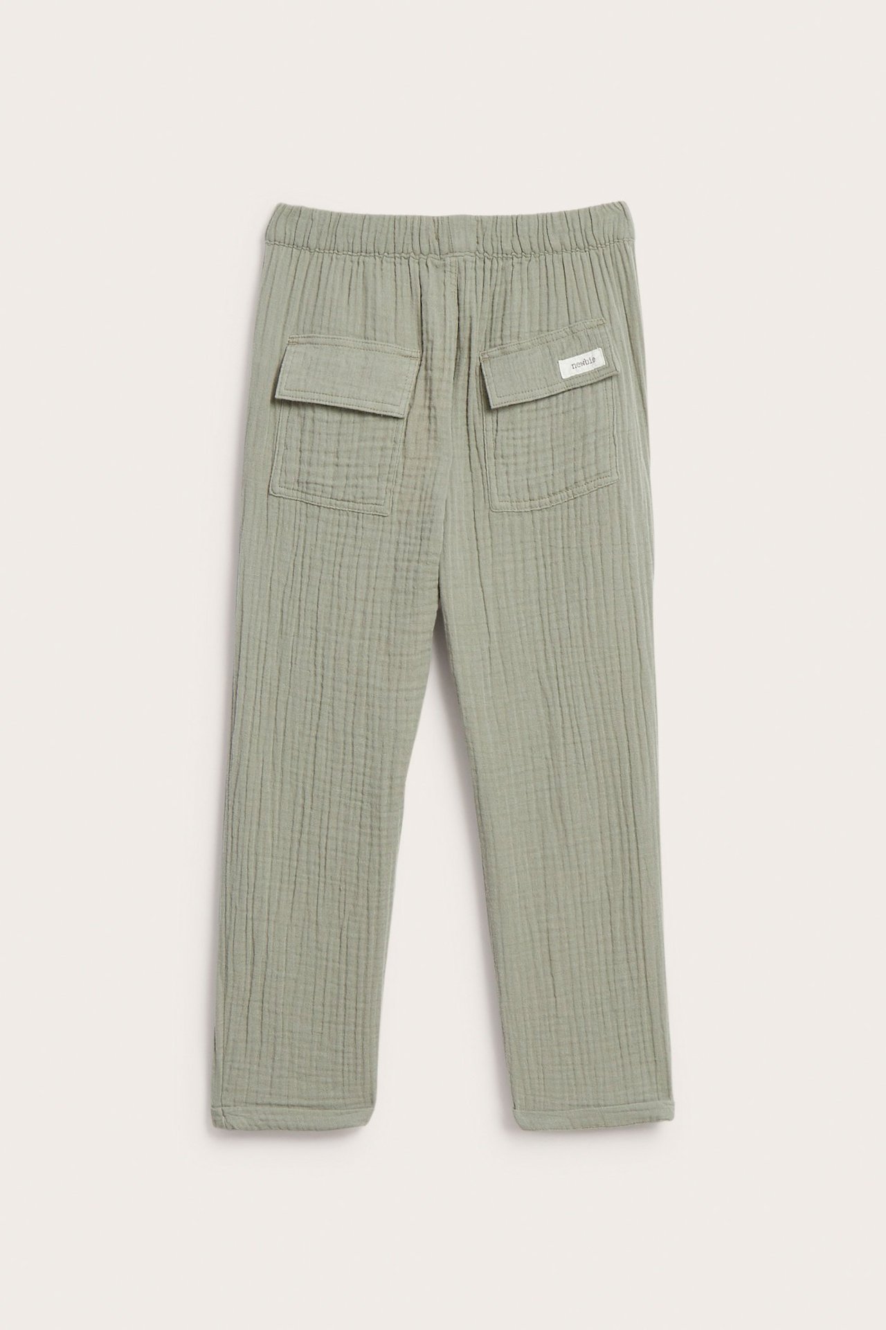 Widok z tyłu dziecięcych spodni z ciemnozielonego muślinu bawełnianego z elastyczną talią i dwiema kieszeniami z klapami.