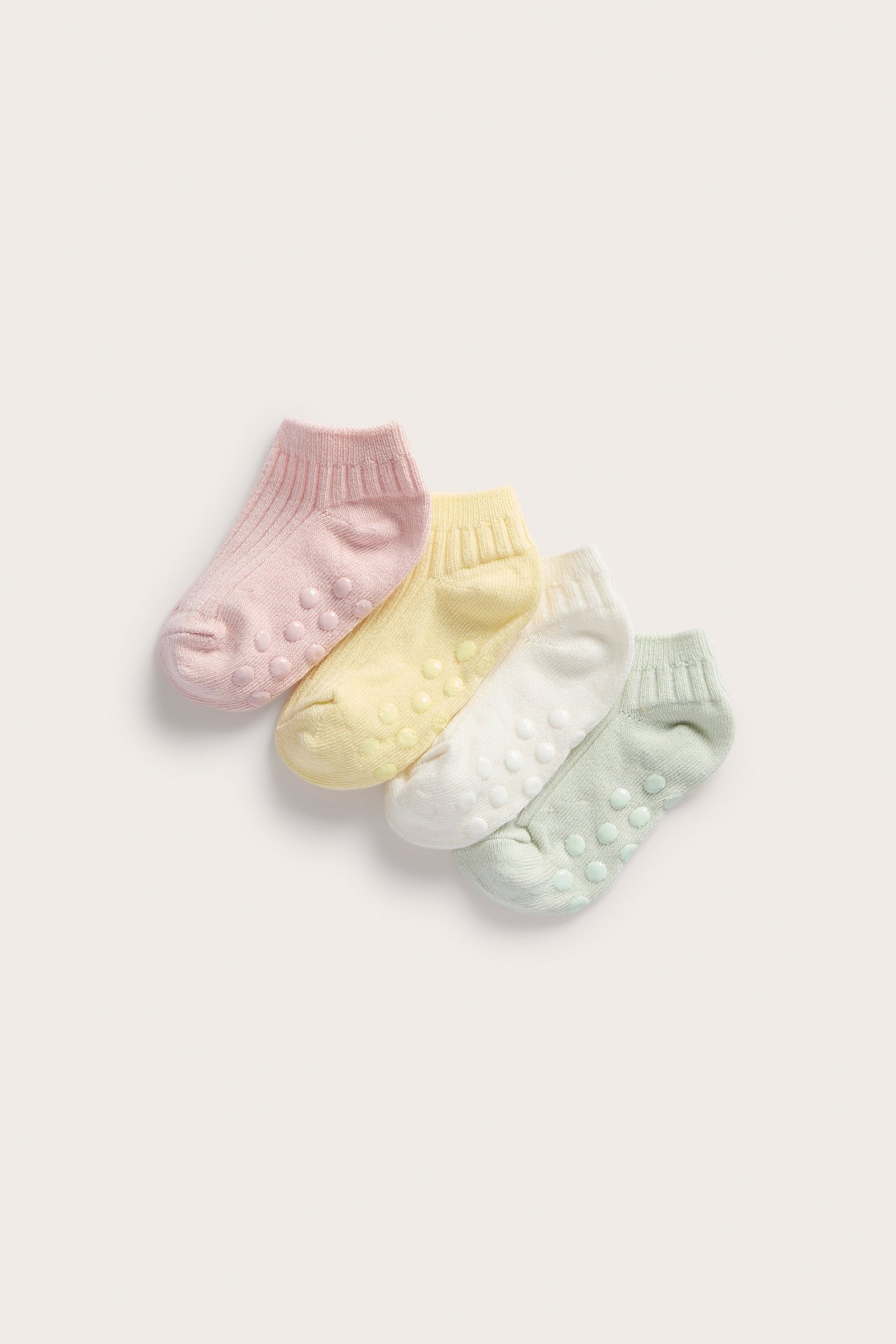 Ovanifrån: fyra ribbade halkskyddsstrumpor för baby i rosa, gul, vit och ljusgrön.