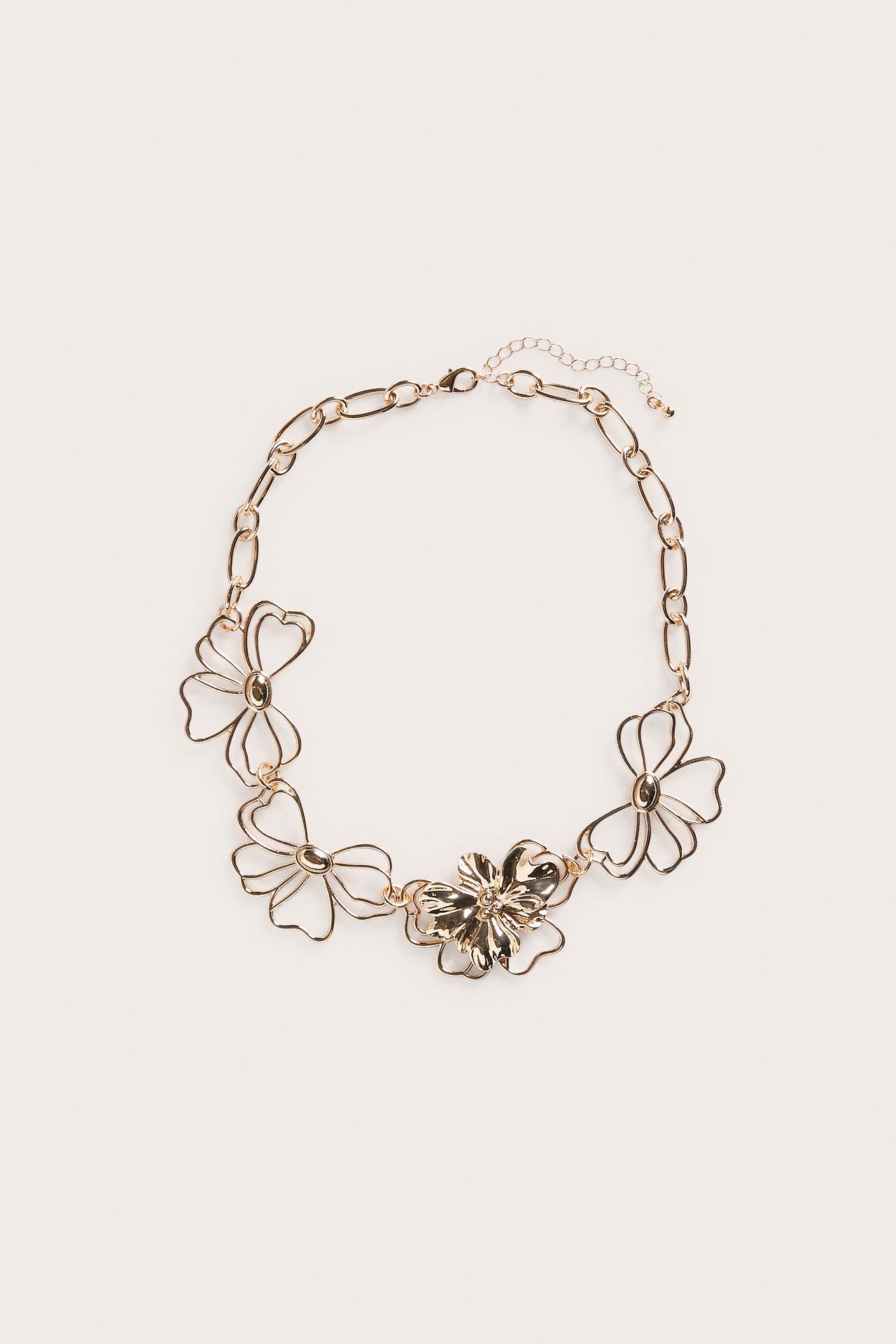 Ylhäältä kuvattu kultavärinen metallikaulakoru, jossa on kukka-aiheita ja papukaijalukko.
