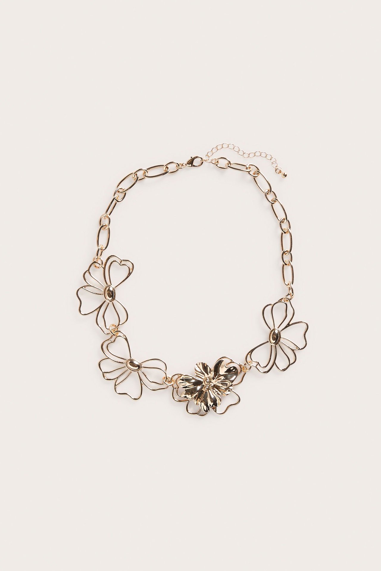 Ylhäältä kuvattu kultavärinen metallikaulakoru, jossa on kukka-aiheita ja papukaijalukko.
