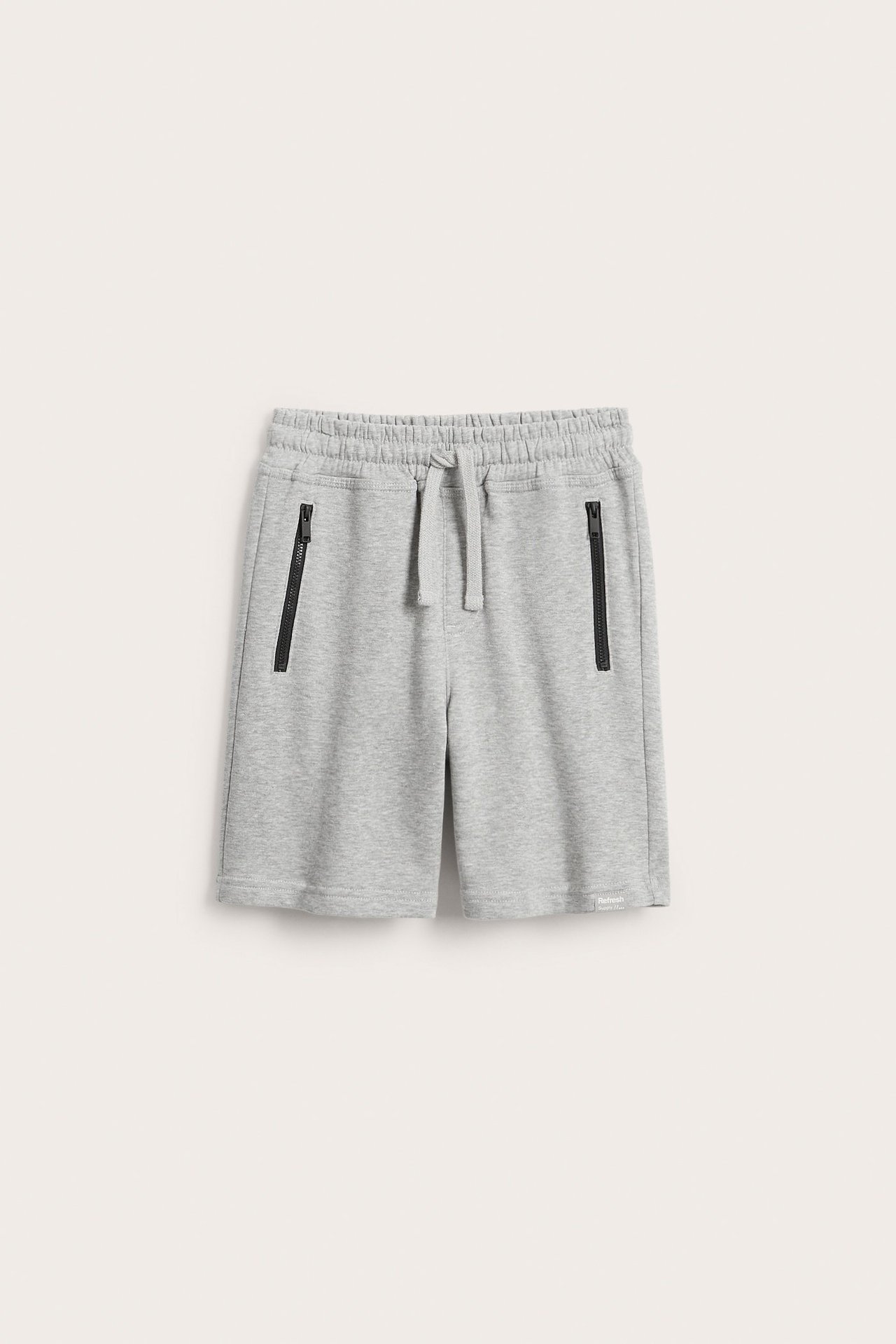 Frontvy av barnens ljusgråmelerade sweatshorts i bomullstrikå med dragsko och svarta dragkedjefickor.