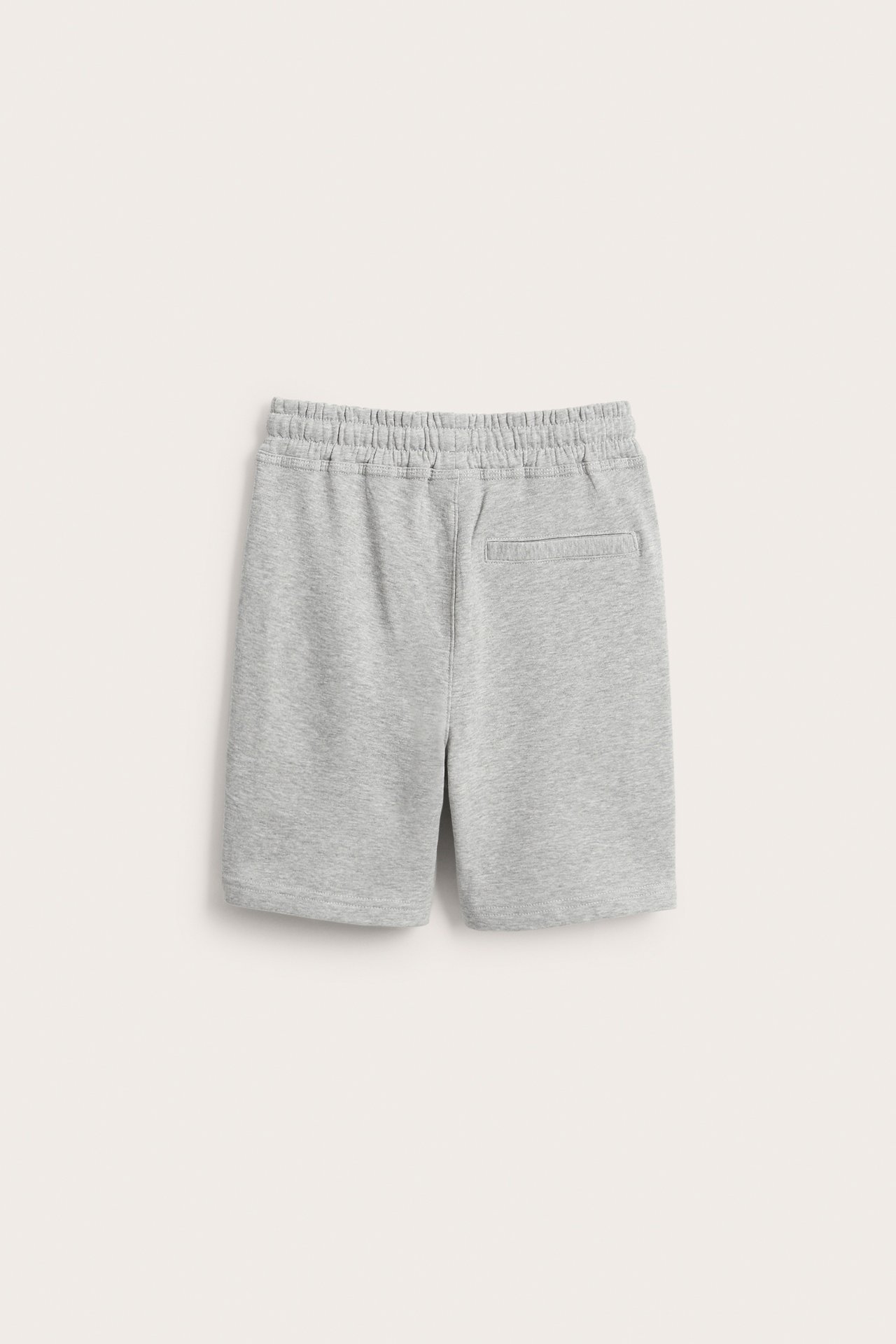 Bakvy av ljusgråmelerade mjukisshorts för barn med resår i midjan och en bakficka.