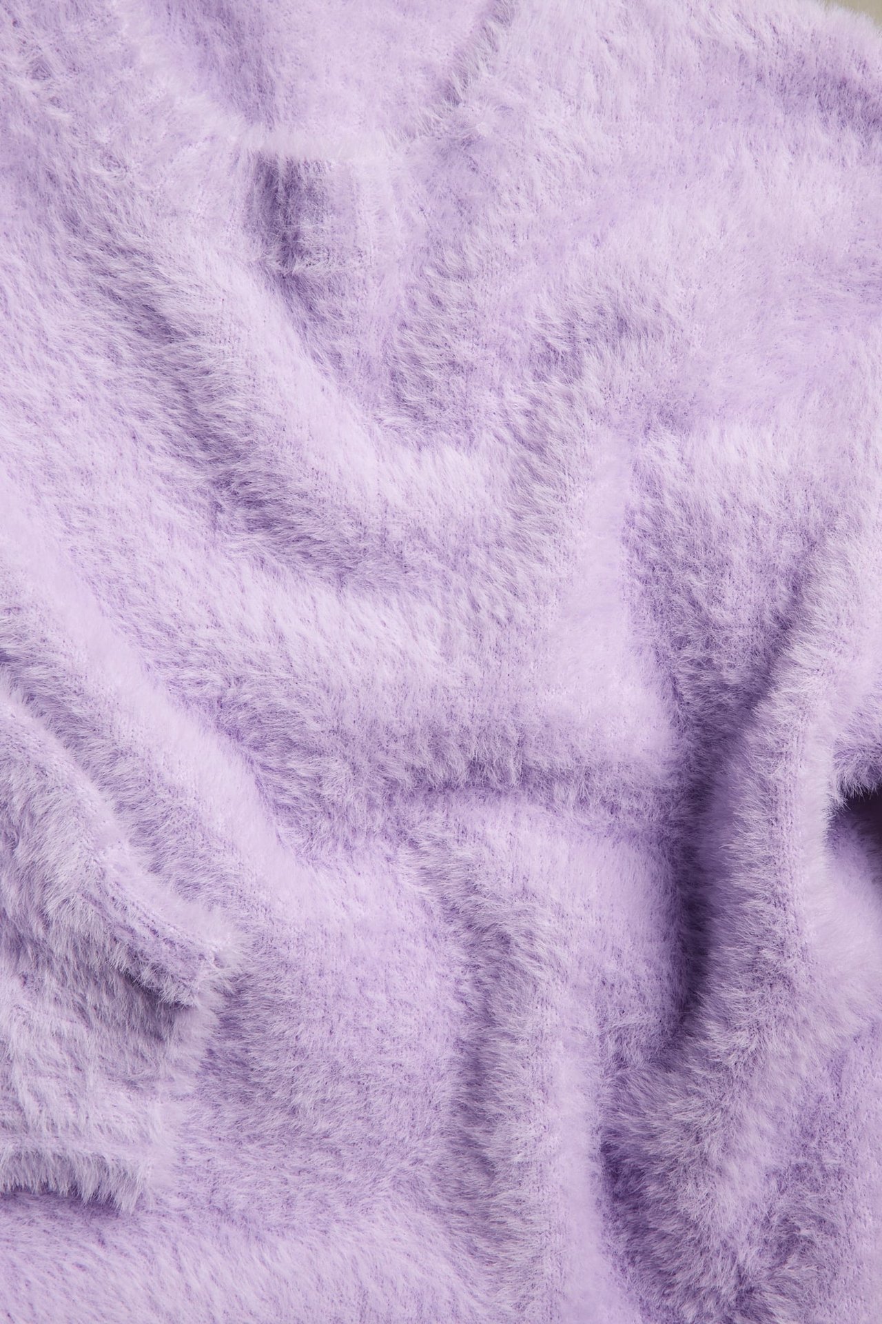 Zbliżenie na jasnofioletowy puszysty sweter z dzianiny z widocznymi zagnieceniami.