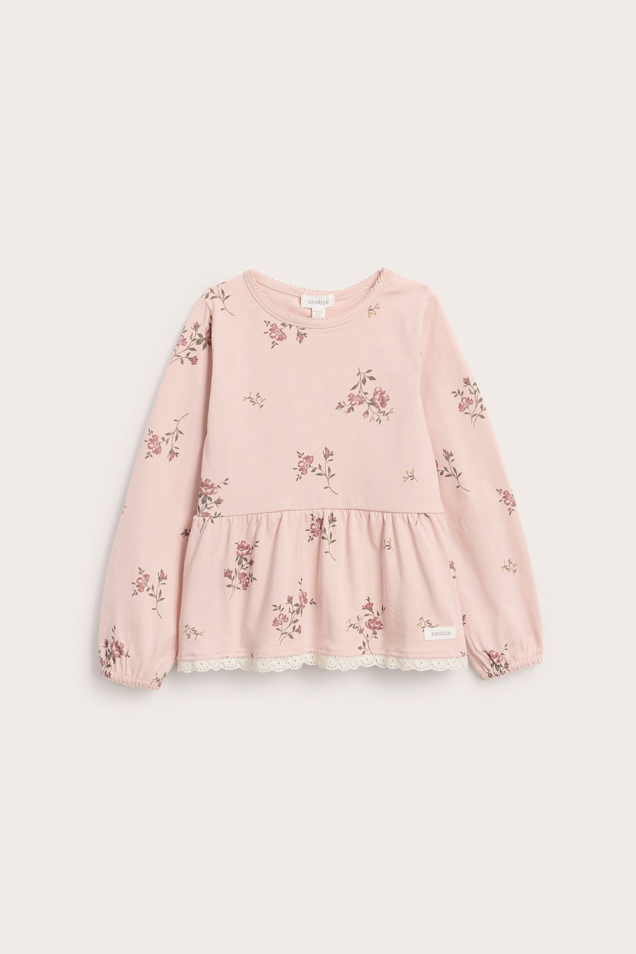 Edestä kuvattu lasten vaaleanpunainen kukkatoppi, pitkähihainen peplum-malli, joustavat hihansuut, pitsireuna.