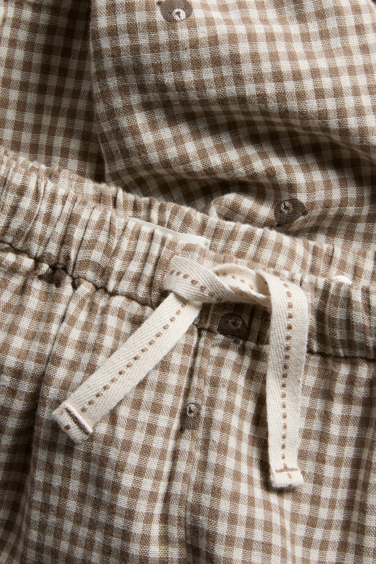 Närbild på bruna och vita gingham-pyjamasbyxor med björnmönster och dragsko i midjan.