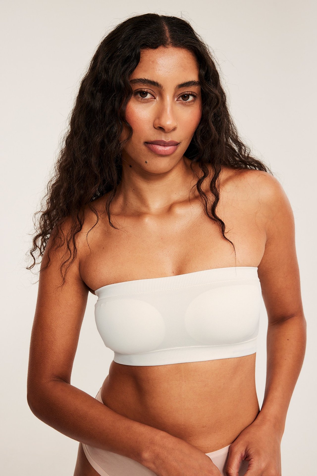 Framifrån, kvinna i vit sömlös bandeau-bh med ribbade kanter och ljusrosa sömlösa trosor.
