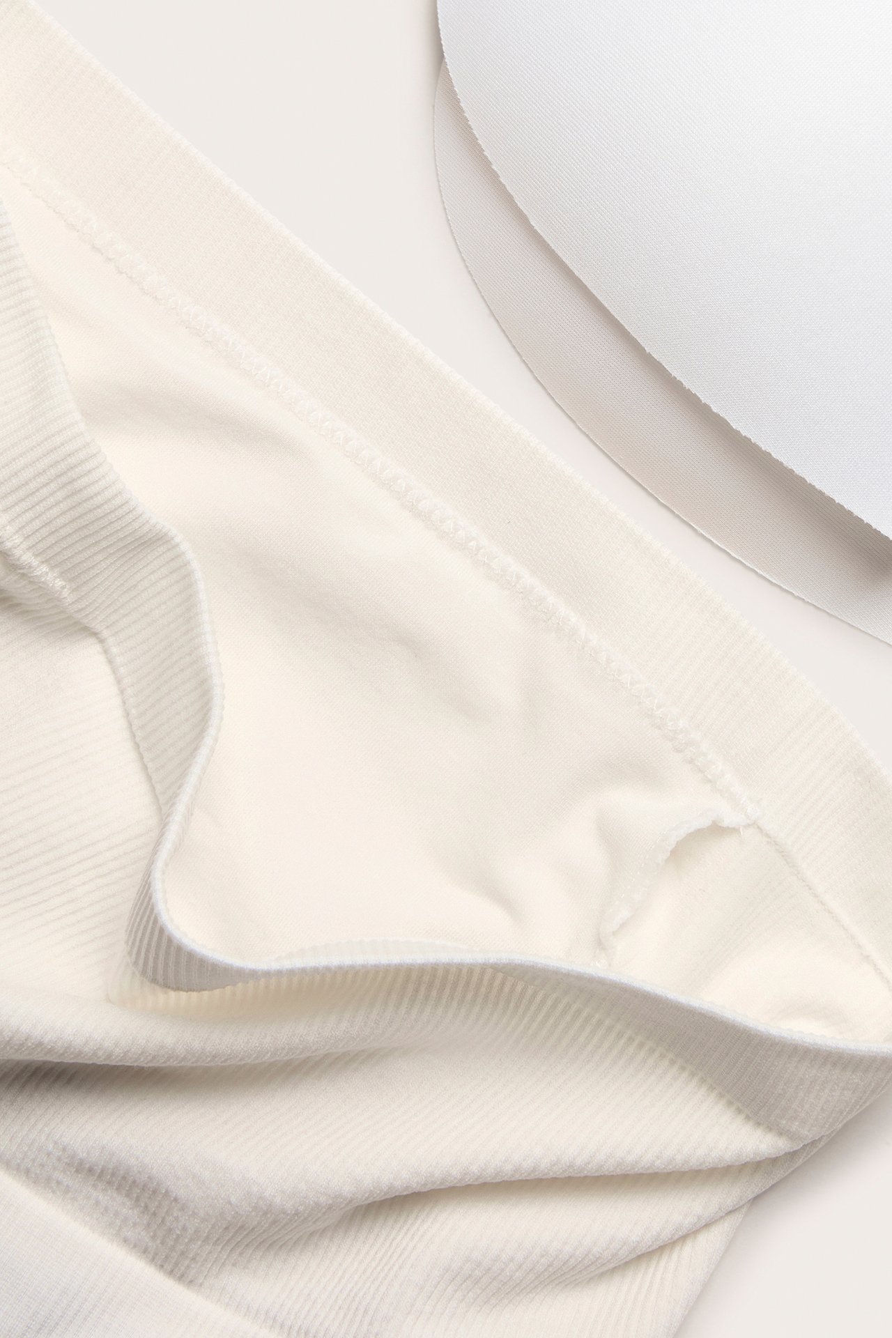 Närbild på en vit sömlös bandeau-bh med ribbade detaljer, som visar dess mjuka tyg och två vita bh-inlägg.