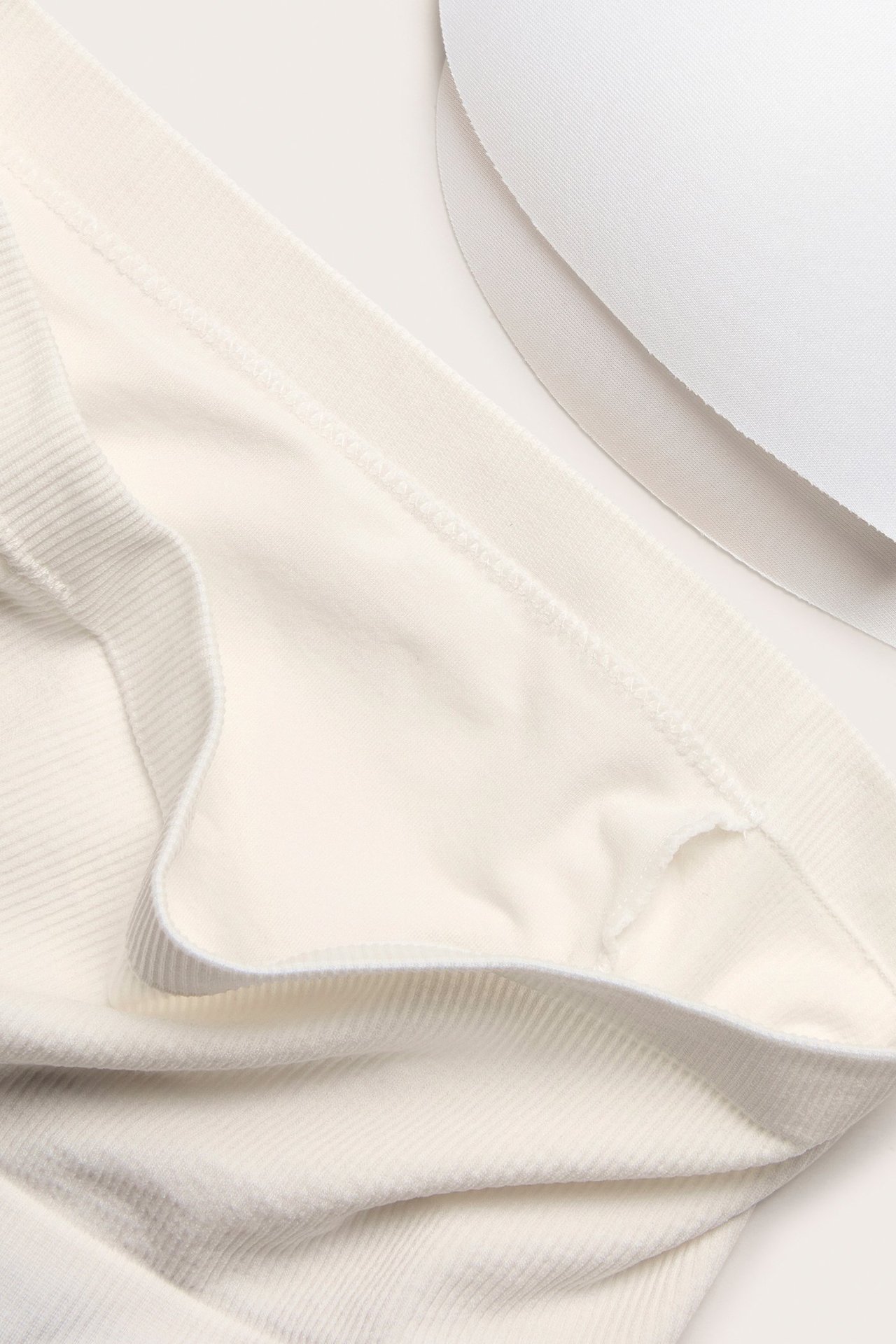 Närbild på en vit sömlös bandeau-bh med ribbade detaljer, som visar dess mjuka tyg och två vita bh-inlägg.