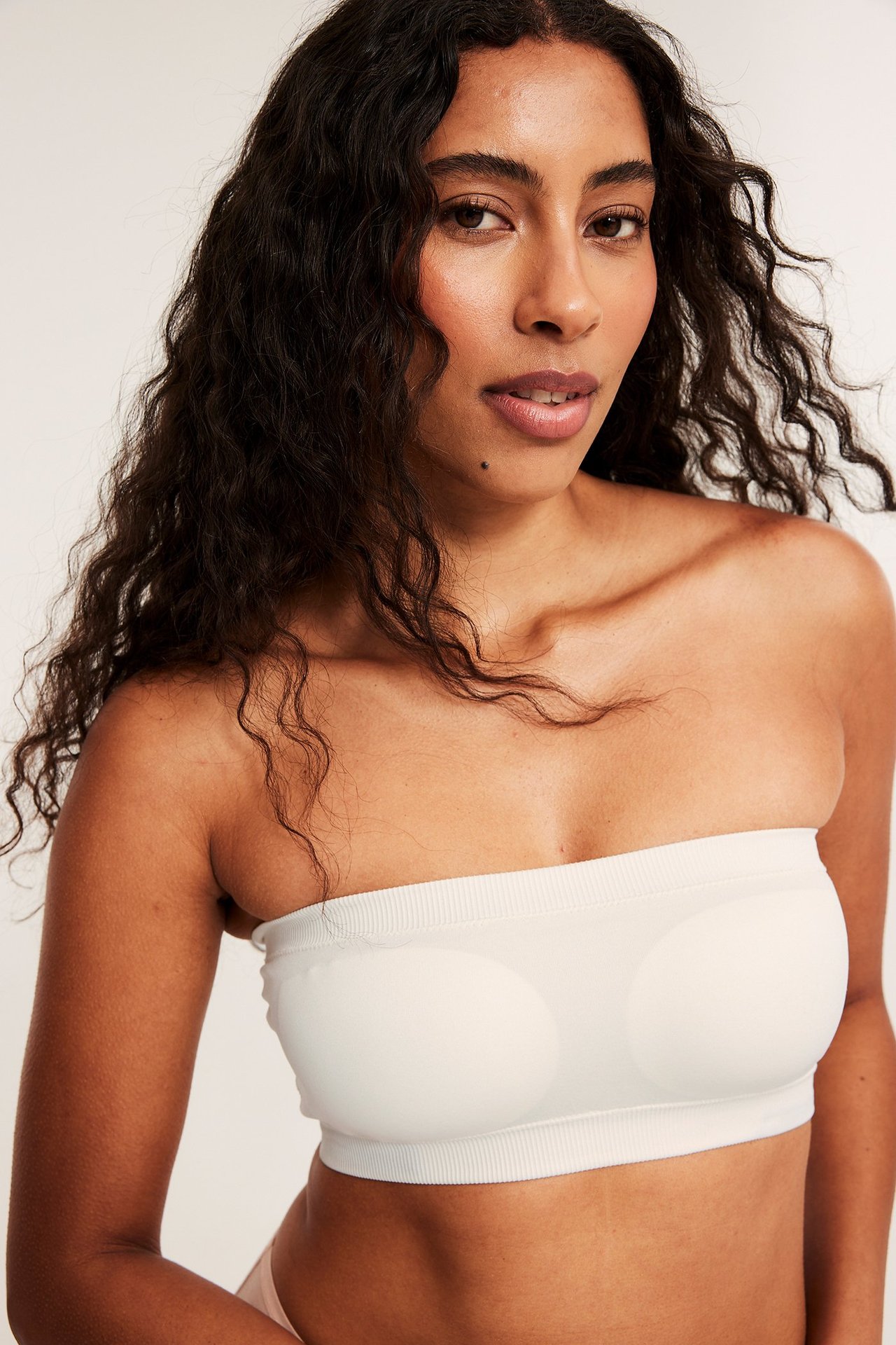 Framifrån, kvinna bär en vit sömlös bandeau-bh med ribbade kanter och synlig vaddering.