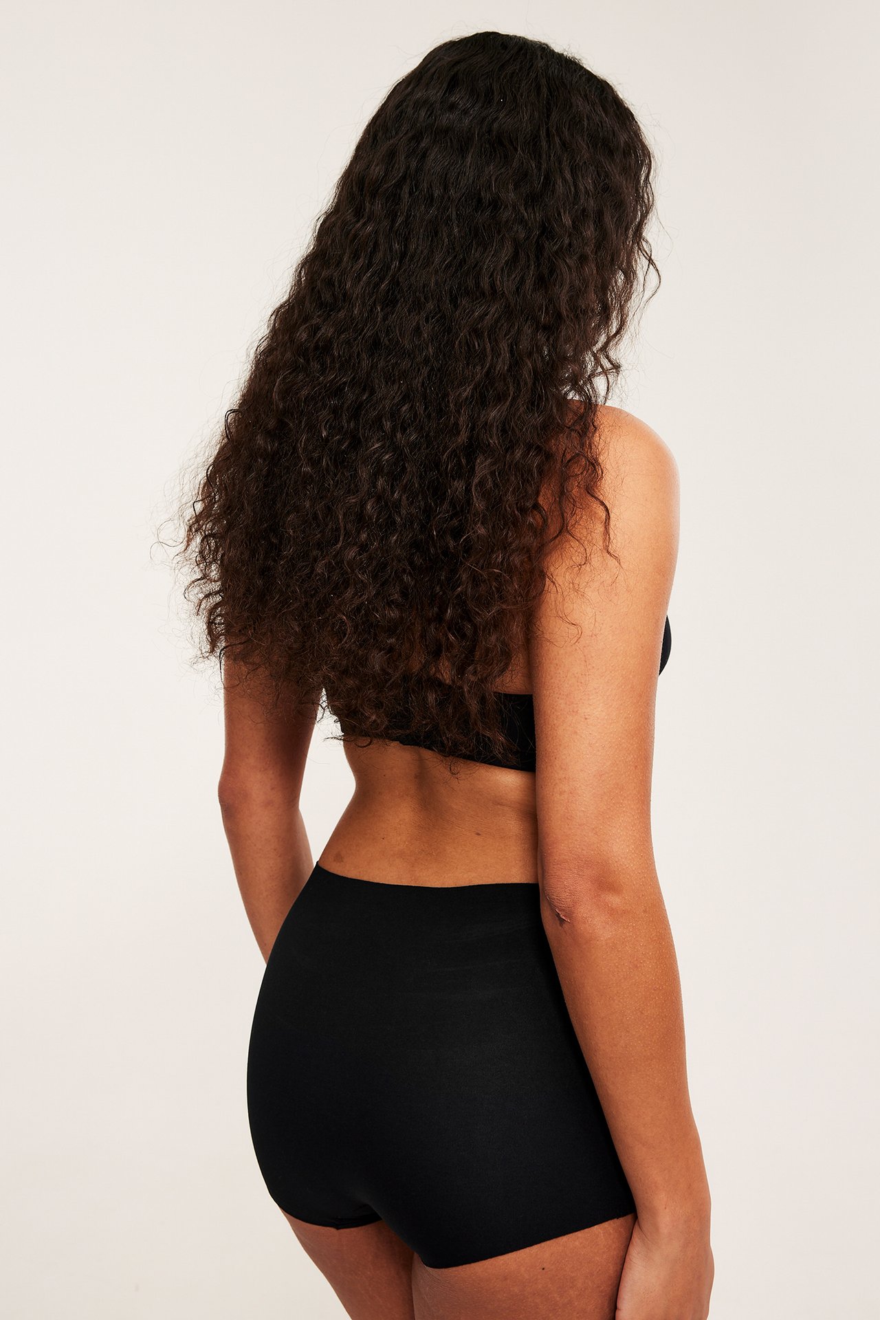 Bakfra bilde av kvinne med svart amme-bh i bomull og svart undertøy.