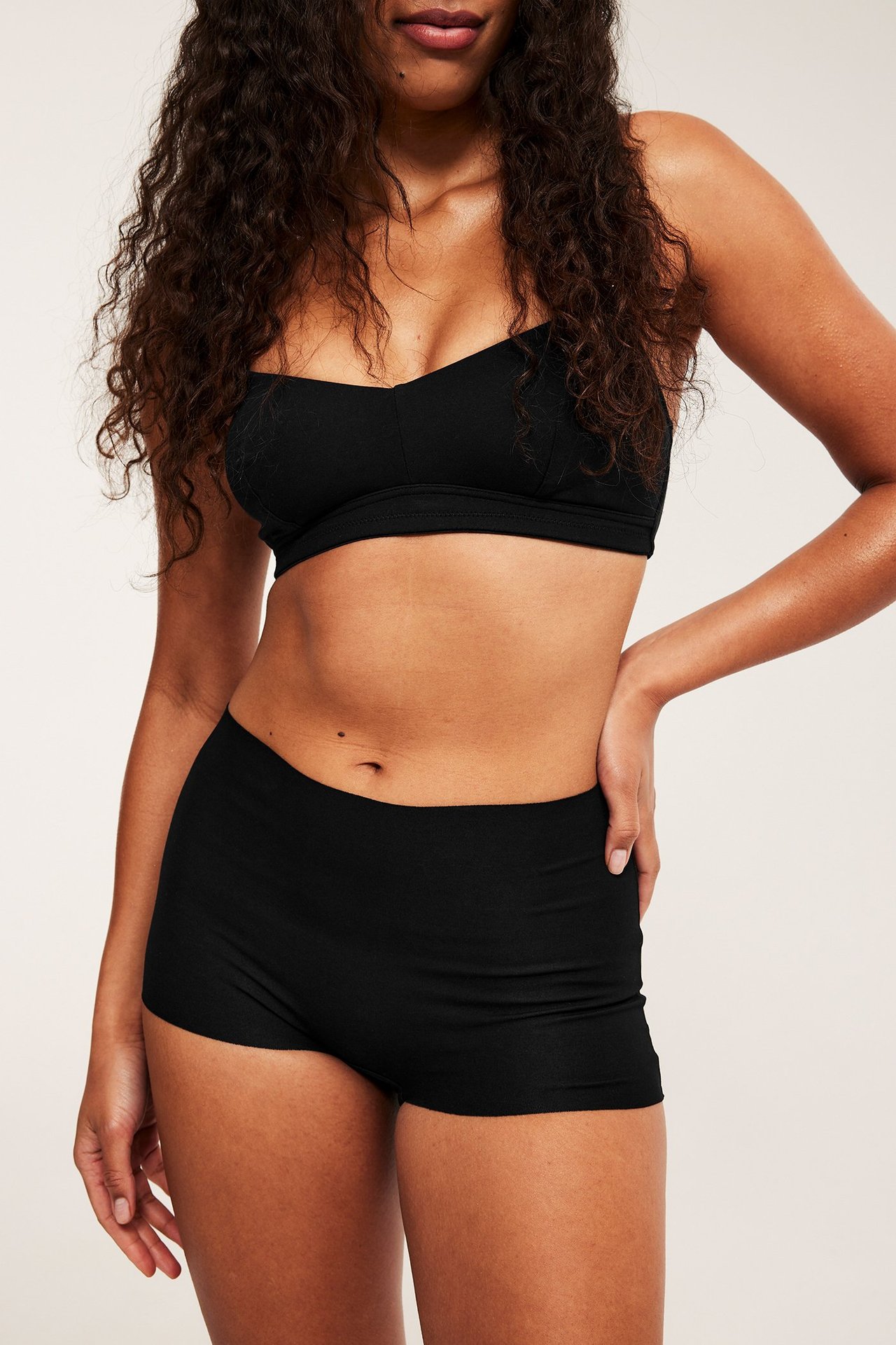 Frontvy av en kvinna i en svart, mjuk amnings-bh i bomull och matchande svarta shorts.