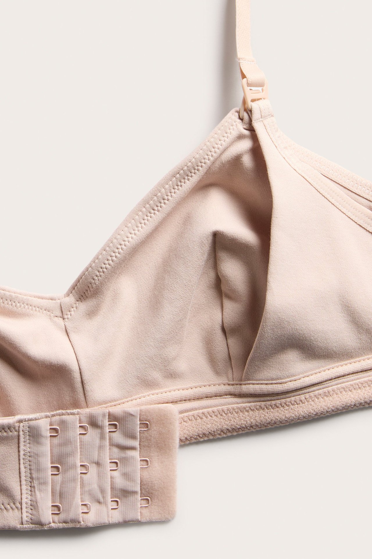 Lähikuva vaaleanpunaisesta puuvillaisesta imetysliivistä, jossa on imetysklipsi ja useita hakas- ja silmukkakiinnikkeitä.