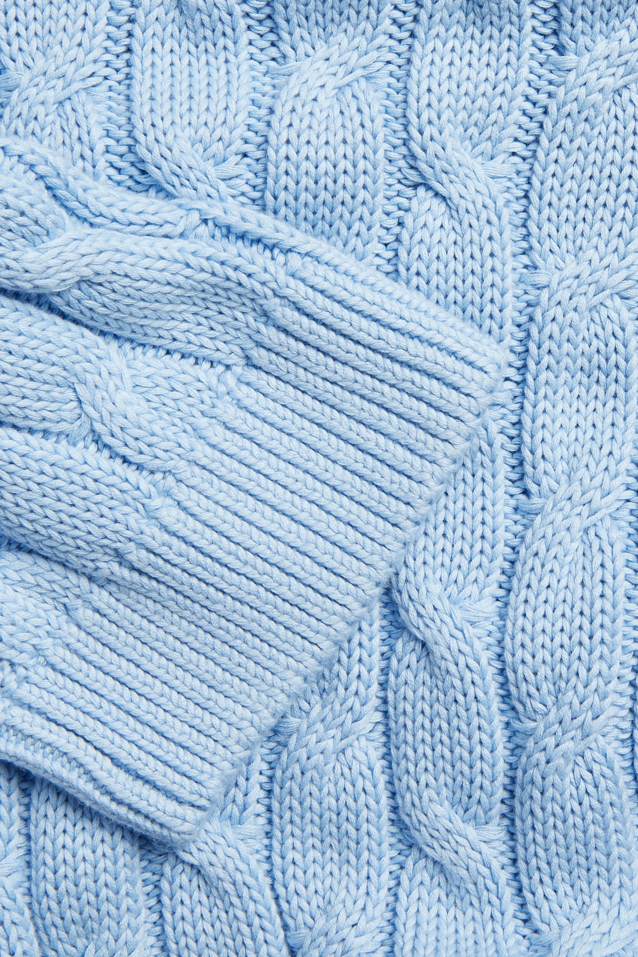 Lähikuva vaaleansinisestä palmikkoneulotusta puuvillaneuleesta, jossa on ribbireuna.