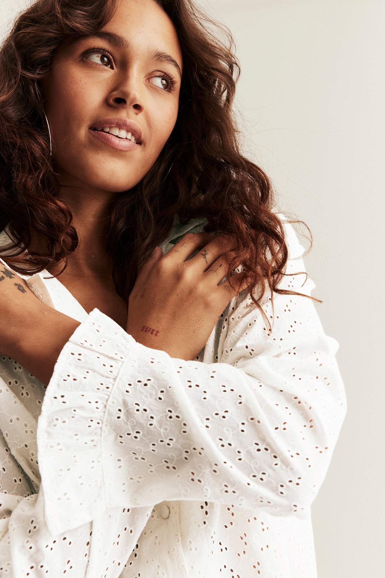 Närbild av kvinna i offwhite pyjamastopp med broderie anglaise, volanger vid ärmslut och klädda knappar.