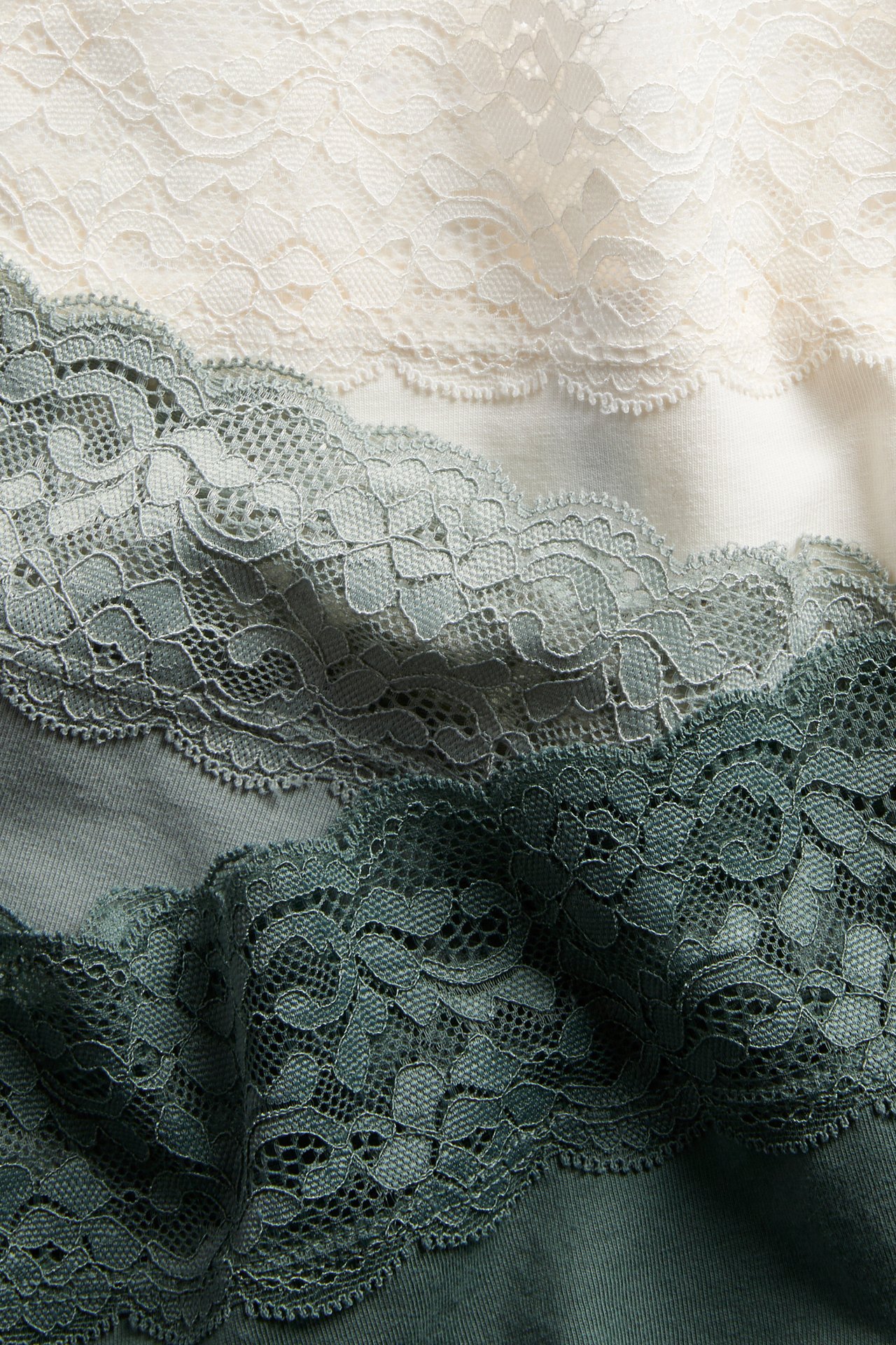 Närbild av tre staplade damhipstertrosor med spetsmidjor i gräddvitt, ljusgrönt och mörkgrönt.