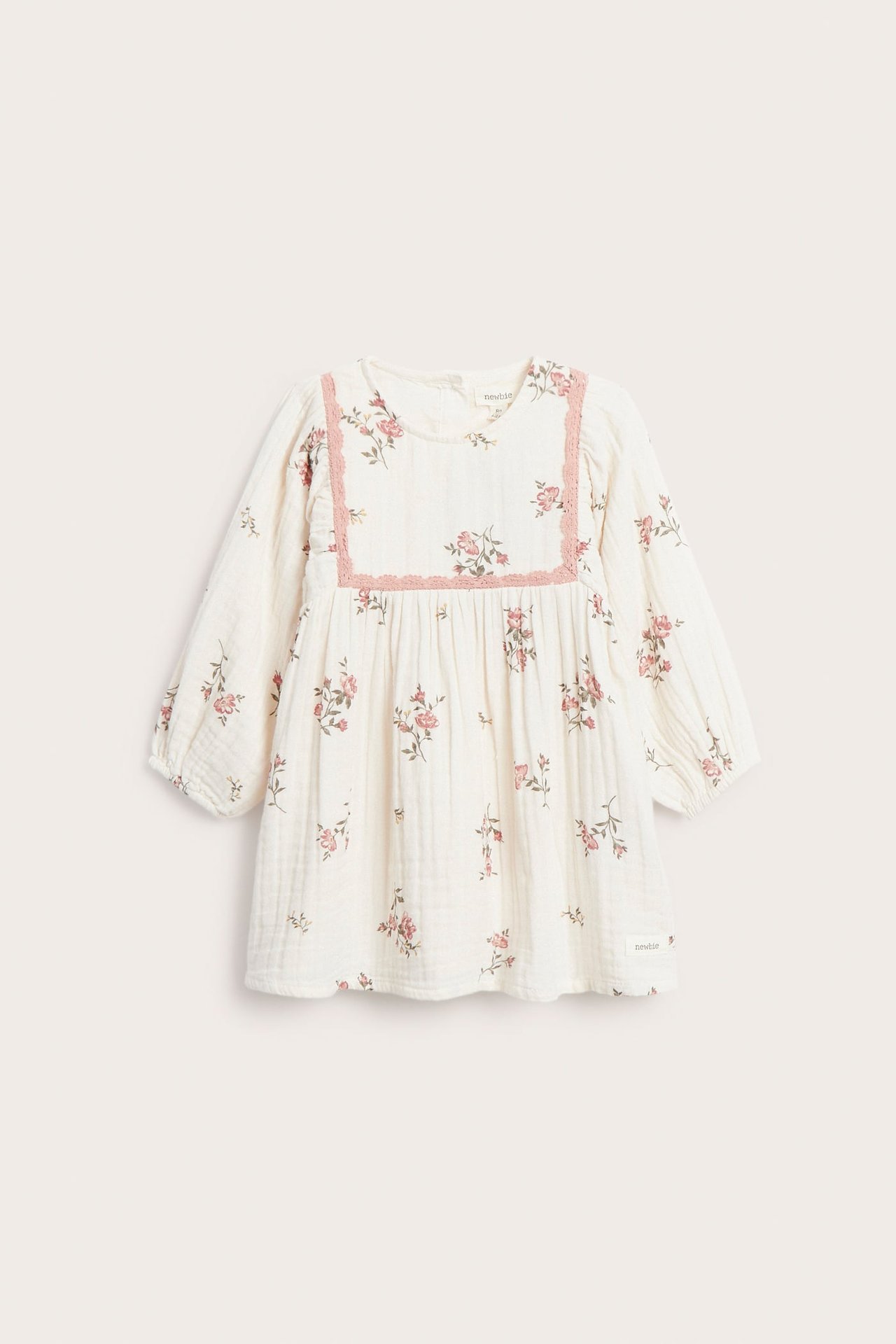 Framsida av offwhite muslin babyklänning med rosa blommönster och rosa spetskant.