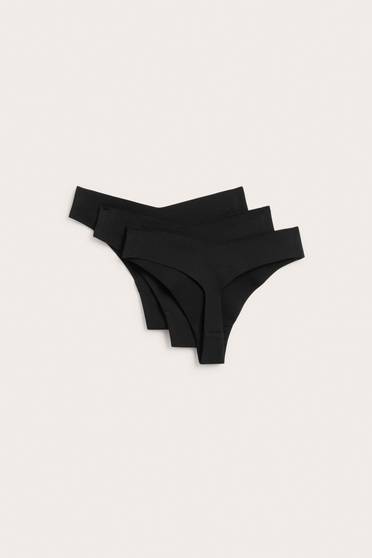 Ovenfra-visning av en 3-pakning svarte sømløse stringtruser i bomullsblanding, stablet og lett spredt.