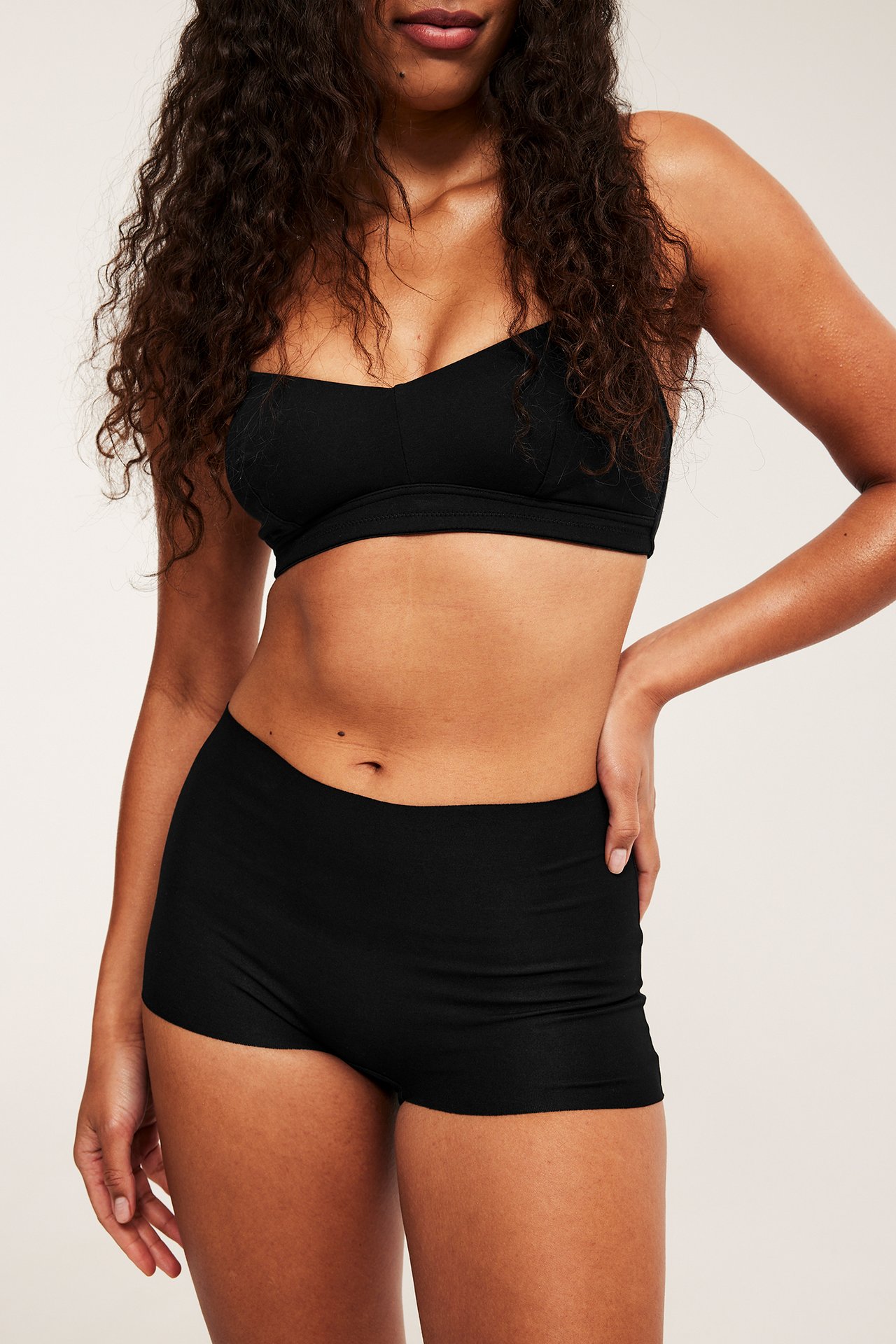 Framifrån, kvinna bär svarta sömlösa boxertrosor i bomullsmix och en matchande svart bralette.