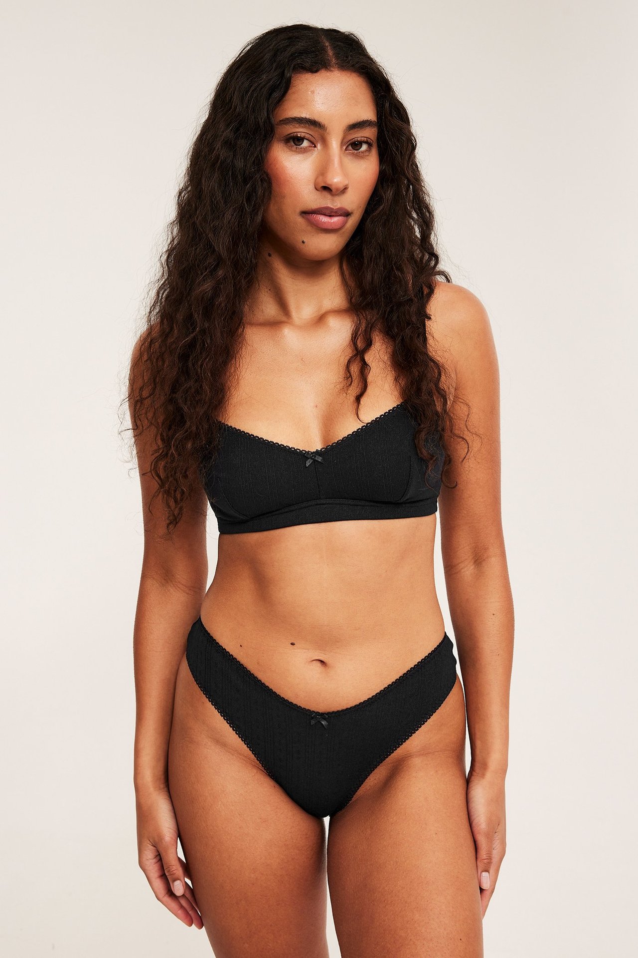 Forfra, kvinne i svarte ribbestrikkede brazilian mammabukser med sløyfe og matchende BH.