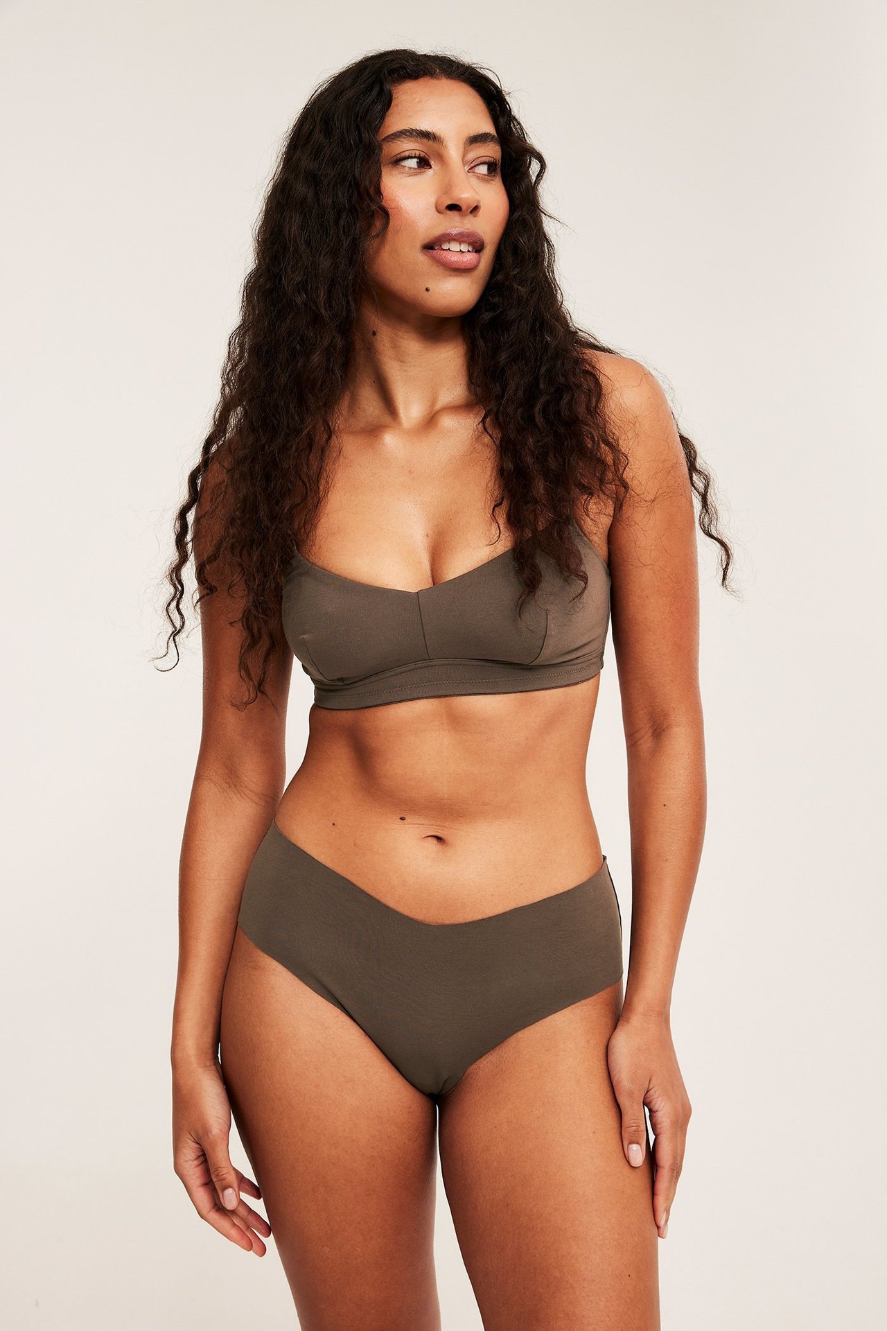 Forfra: kvinne i lavmidjede, sømløse, V-formede mørkegrønne mammatruser og matchende myk BH.