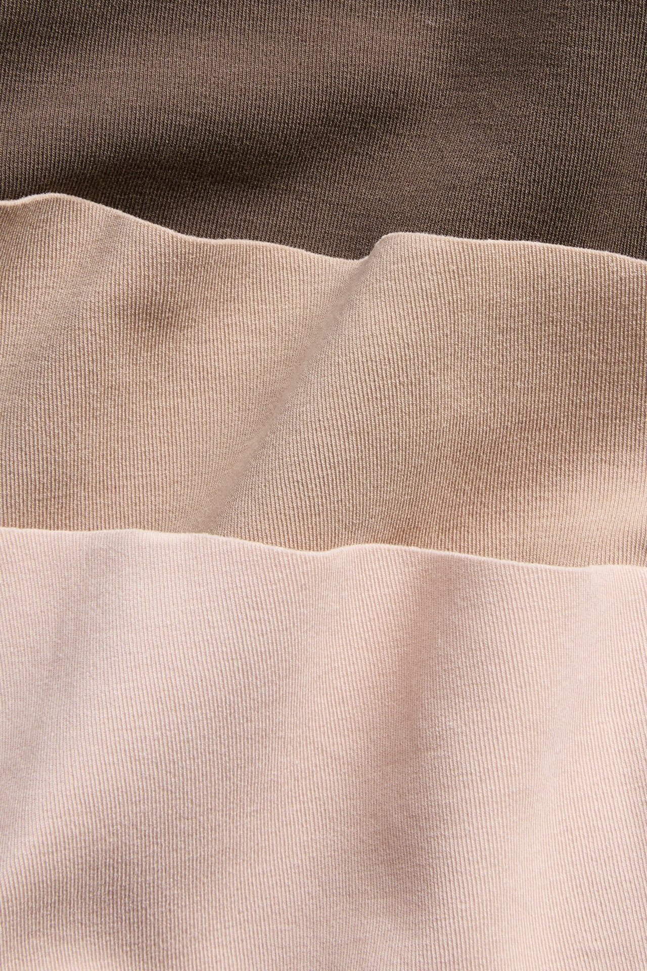 Nærbilde av tre mammatruser i mørkebrun, lys beige og lys rosa bomullsblanding.