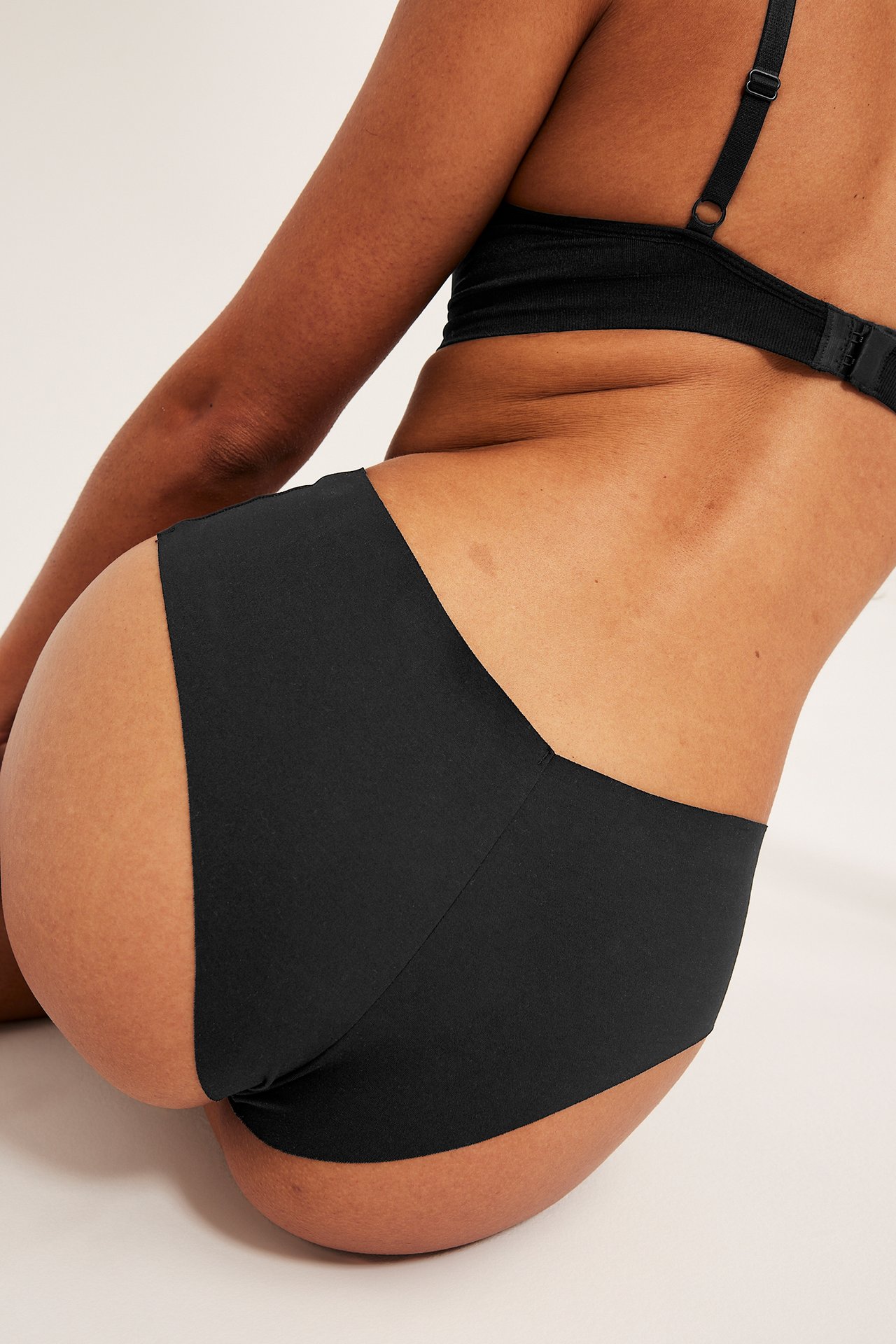 Widok z tyłu boku kobiety w czarnych, bezszwowych, niskich majtkach ciążowych i czarnym biustonoszu.