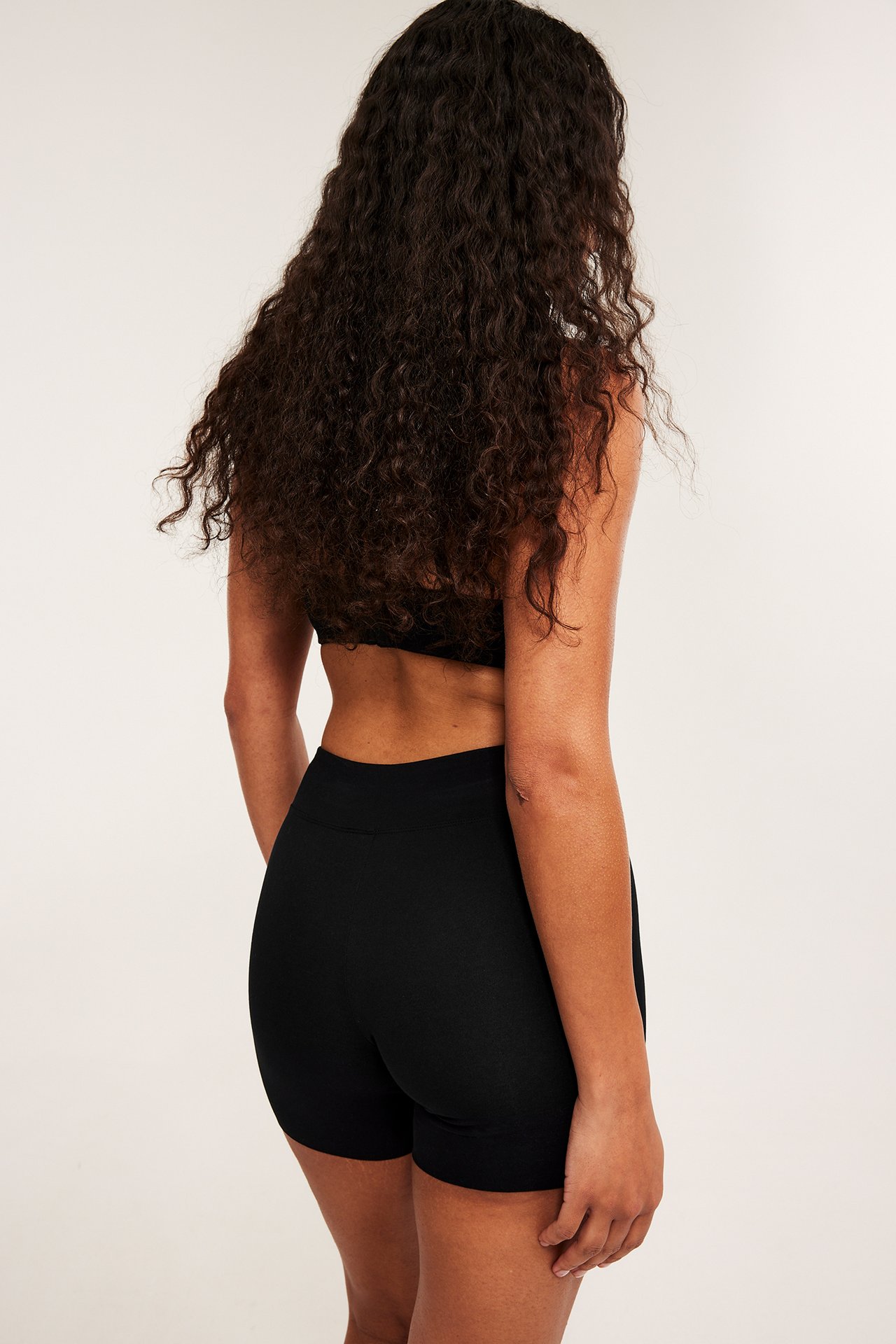 Bakifrån en kvinna i svarta höga bomullsshortstrosor och en svart behåtopp.