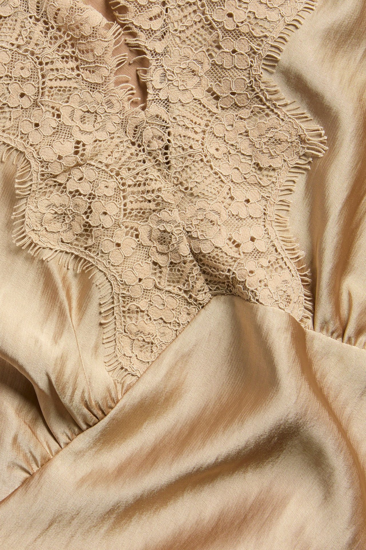 Zbliżenie na jasnobrązowy satynowy top z misternymi koronkowymi detalami przy dekolcie.