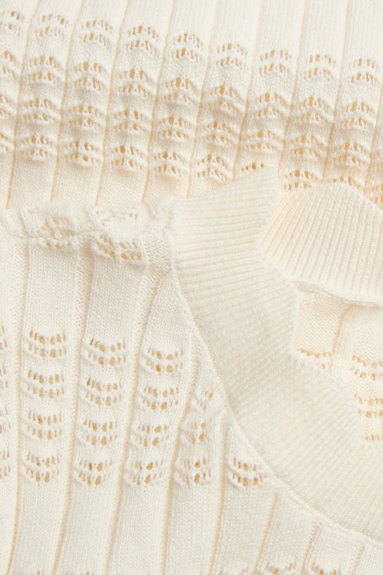 Zbliżenie na kremowy bawełniany top z dzianiny o ażurowej strukturze i prążkowanych detalach.