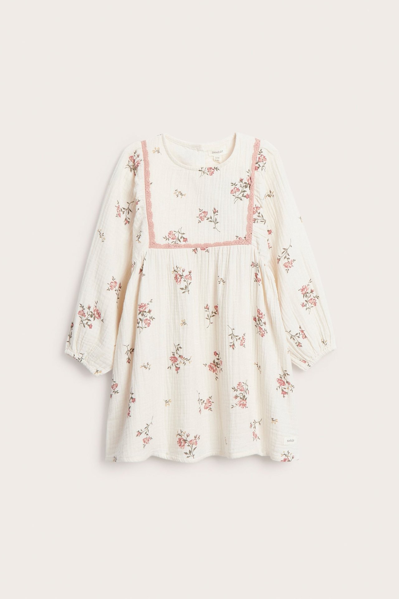 Frontvy av en offwhite blommig klänning i muslin för barn, med långa ärmar och rosa spetskant.