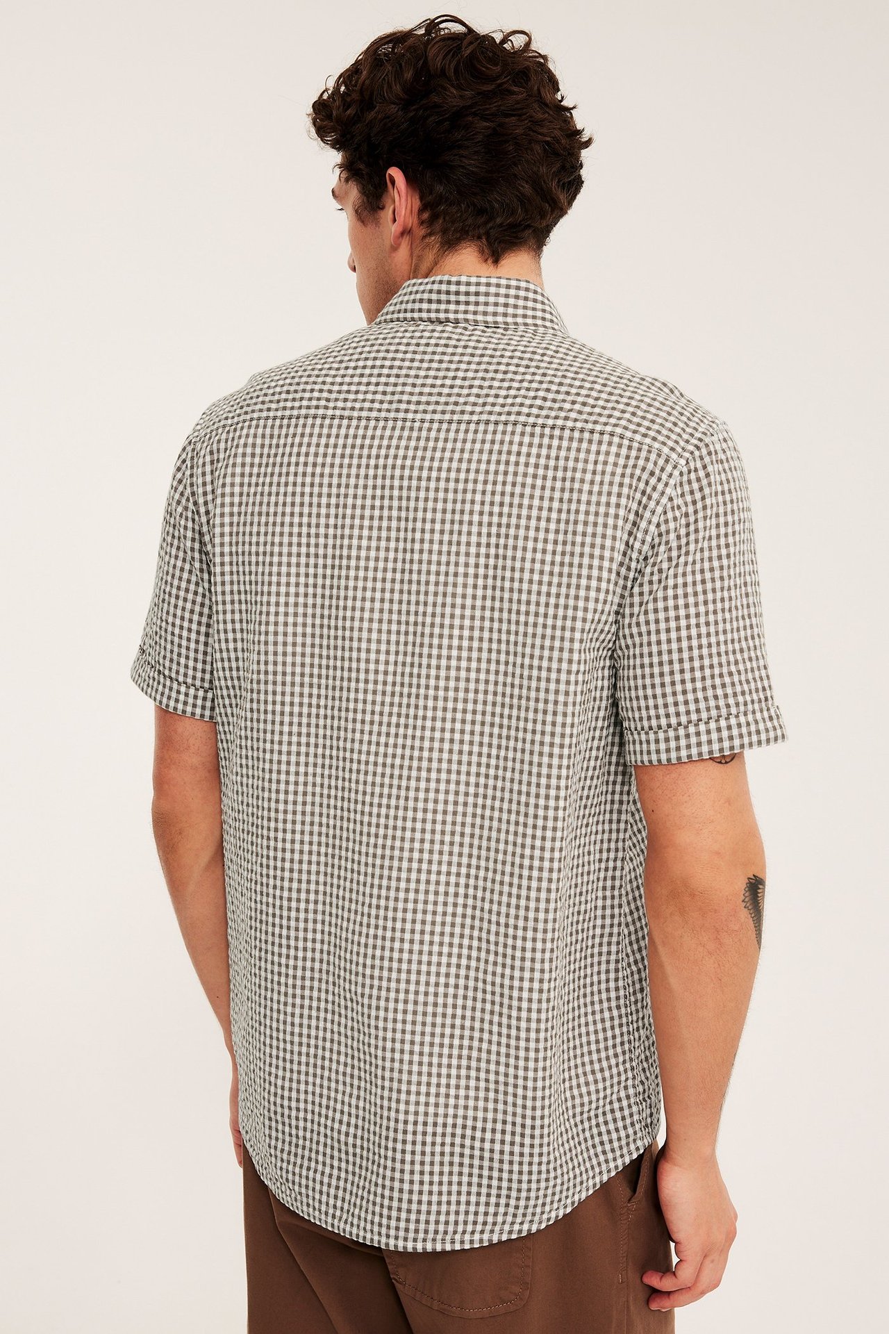 Ryggvy av en man i en ljusbrun- och vitrutig kortärmad bomullsskjorta och bruna byxor.