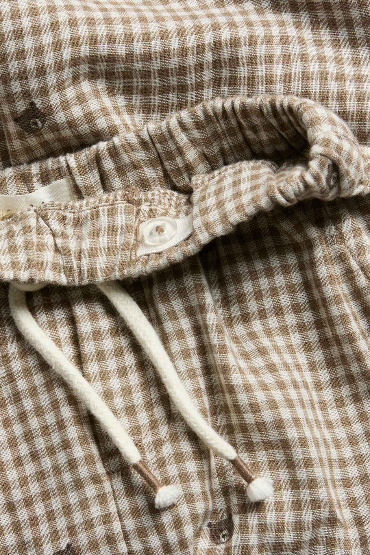 Närbild av bruna och vita rutiga shorts med resår i midjan, knapp, dragsko och björnmönster.