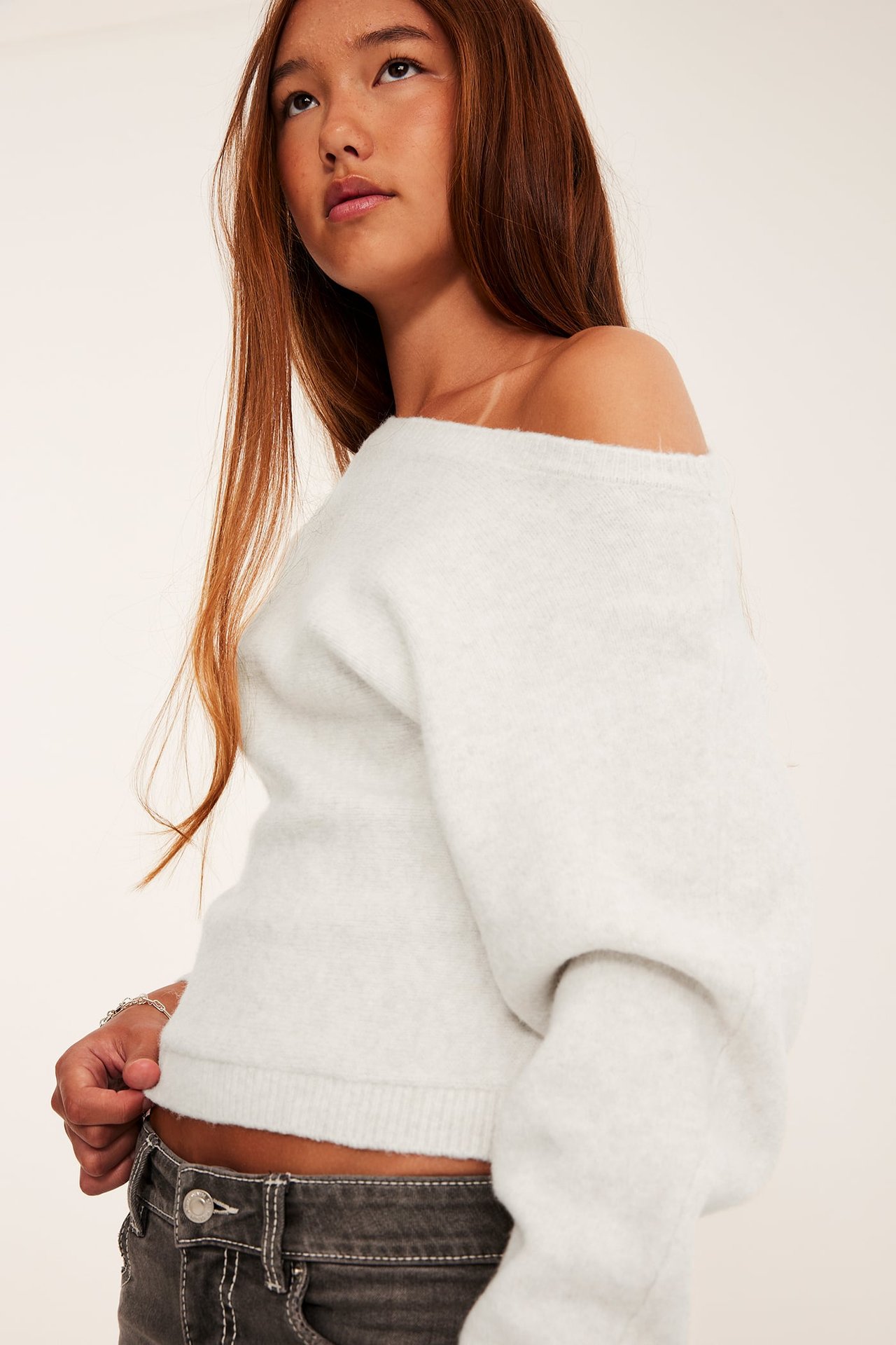 Närbild av kvinna i en off-white off-shoulder-tröja och mörkgrå jeans med vita sömmar.