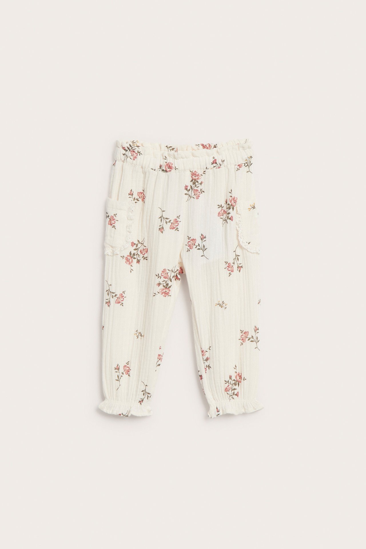 Frontvisning av offwhite blomstrete vevde bukser med blondekantede sidelommer, elastiske mansjetter og midje.