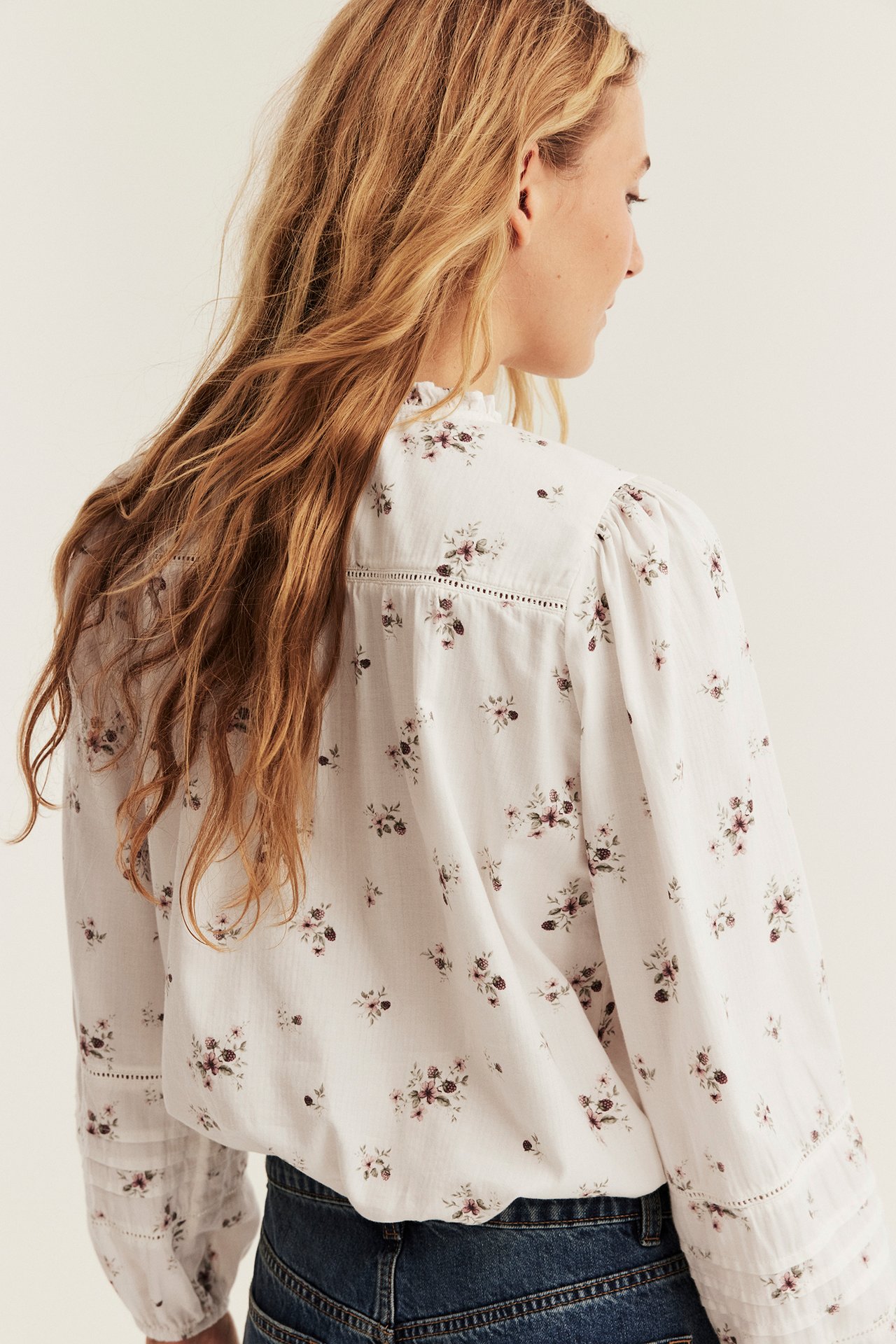 Ryggvisning: Kvinne i hvit blomstret bluse med volangkrage og blå jeans.
