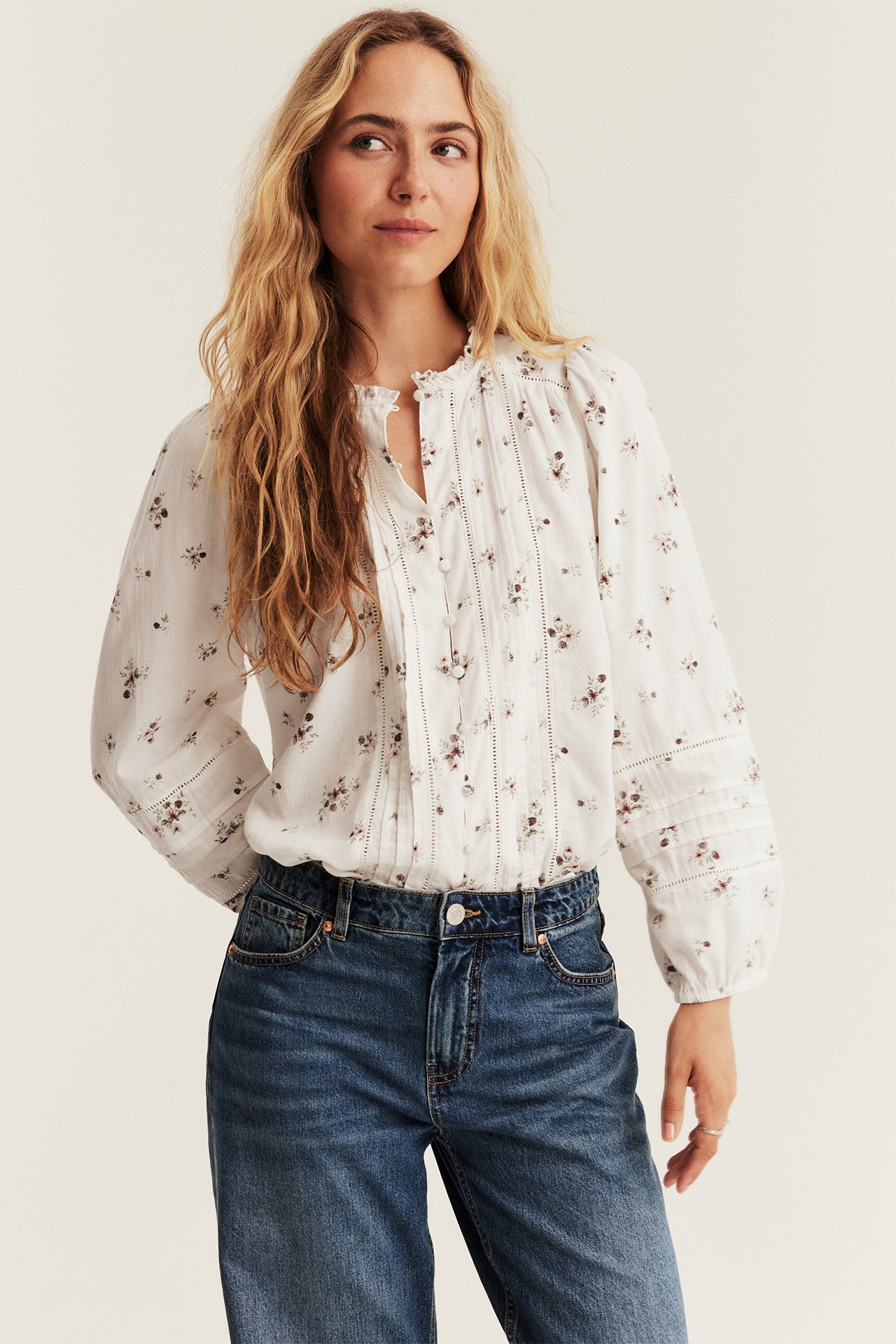 Frontal utsikt av kvinne iført hvit blomstret langermet bluse med legg og blå jeans.