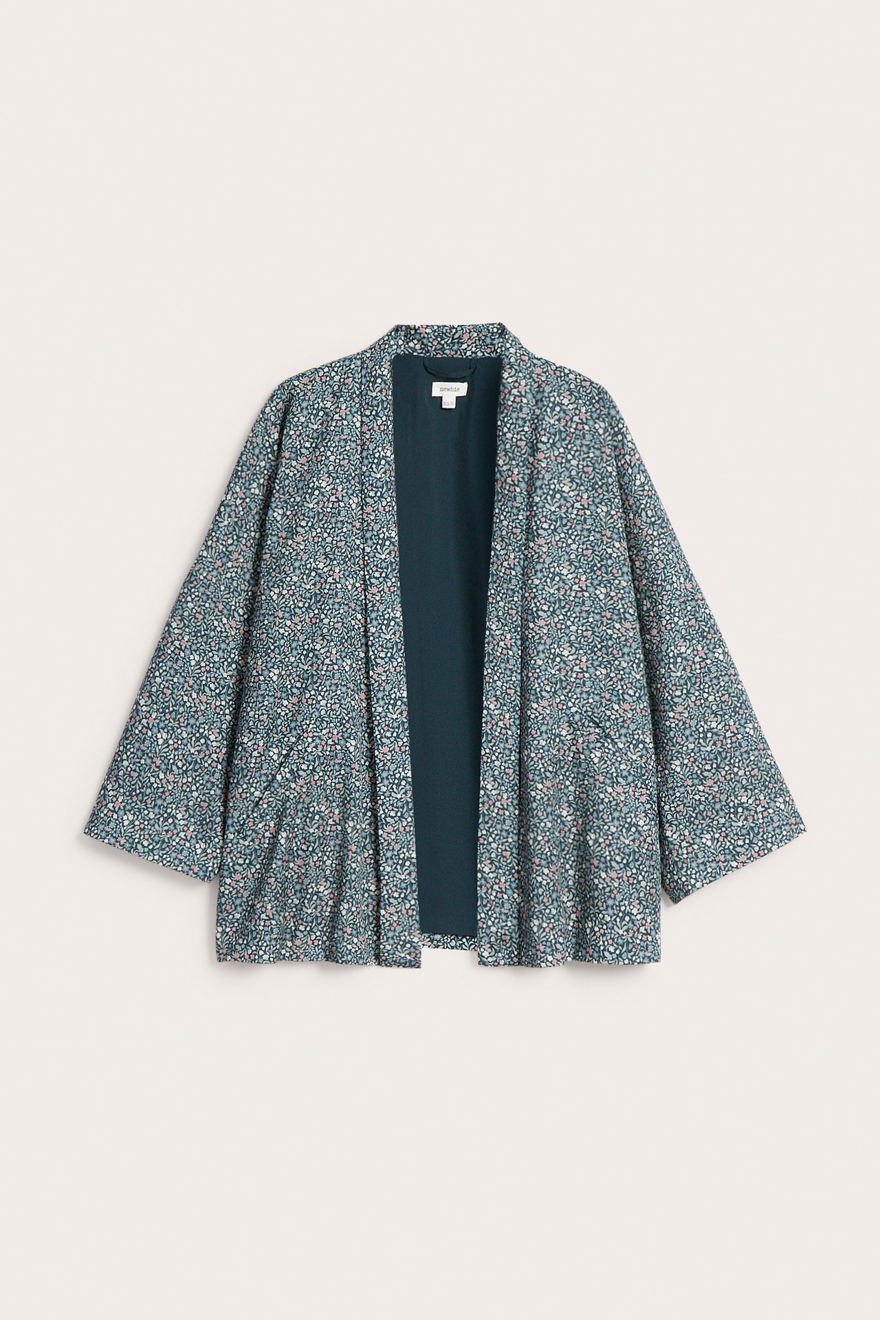 Edestäpäin kuvattu tumman turkoosi kimono-neuletakki, jossa vaaleanpunainen-valkoinen kukkakuvio.