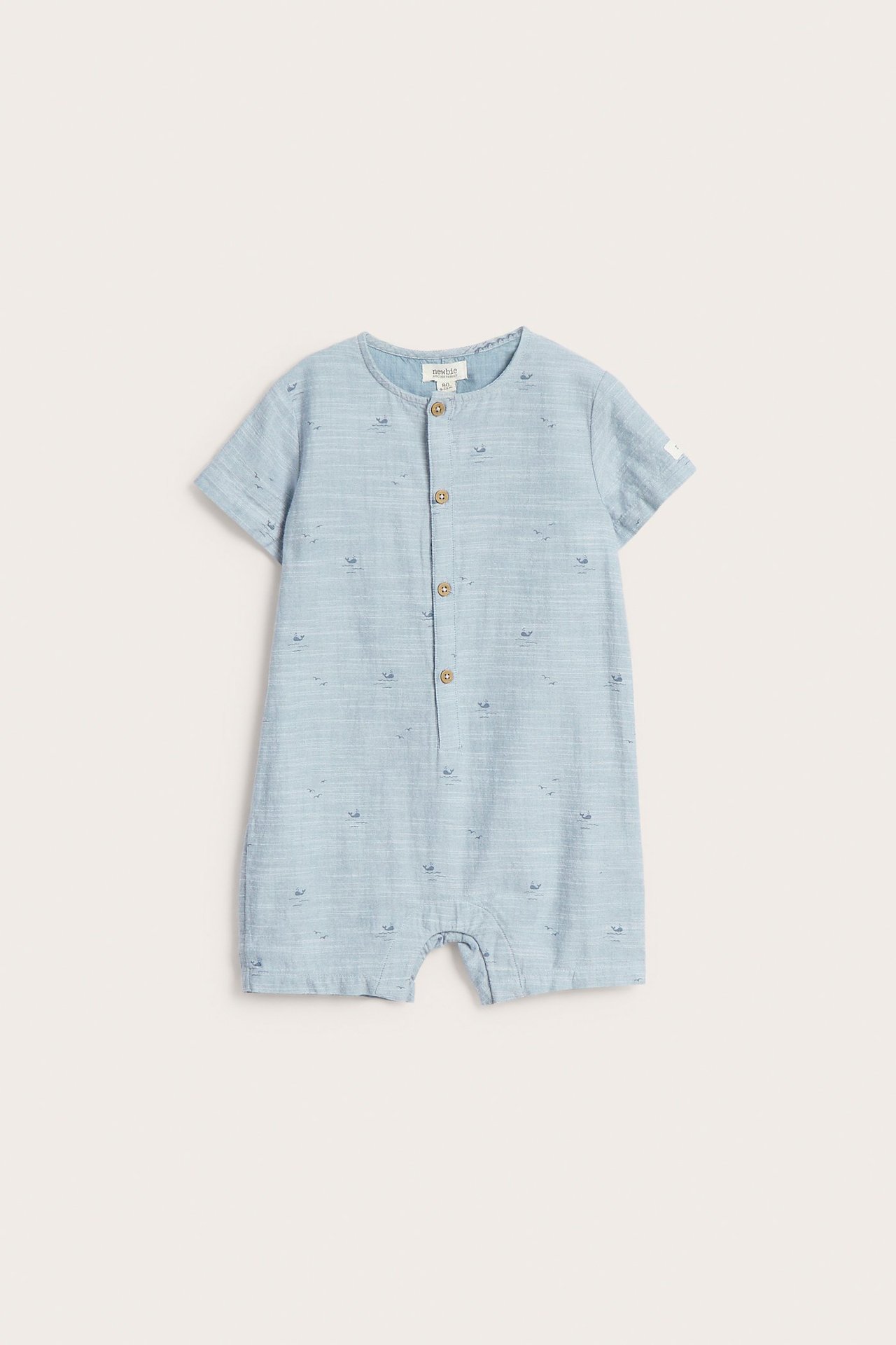 Forfra, blå vevd babyjumpsuit i bomull med hvalmønster og knapper foran.