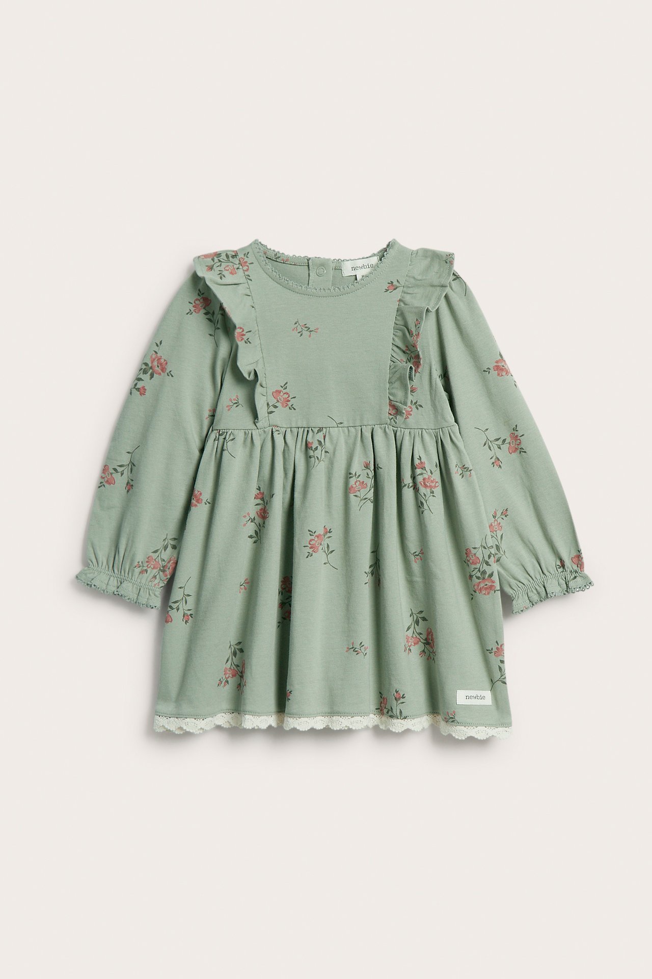 Frontvy av en grön bomullsklänning för baby med rosa blommönster, axelvolanger och vit spetskant.