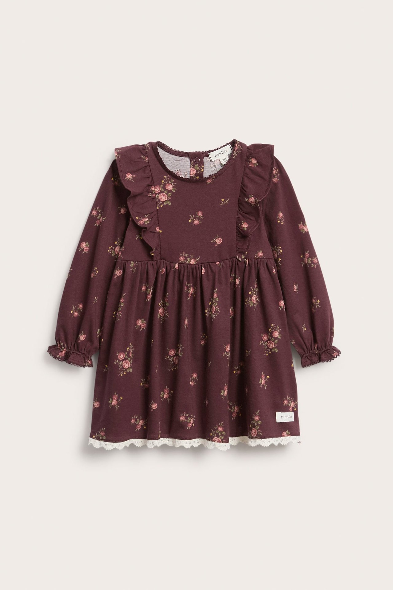 Frontbilde av en vinrød baby-/barneblomstret jerseykjole med skulderkapper og hvit blondekant nederst.