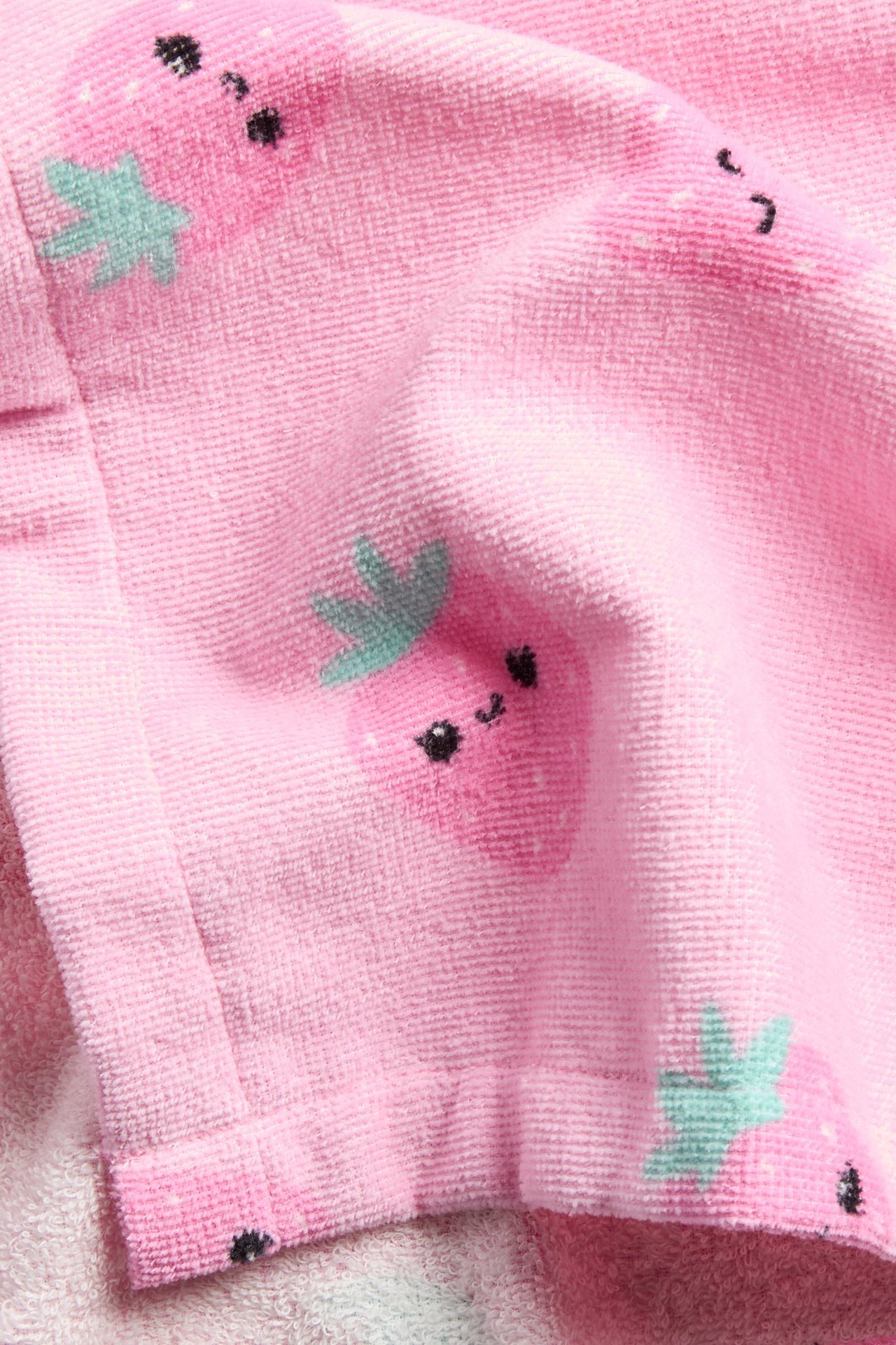 Närbild på en ljusrosa badponcho i bomullsfrotté med upprepat jordgubbsmönster.