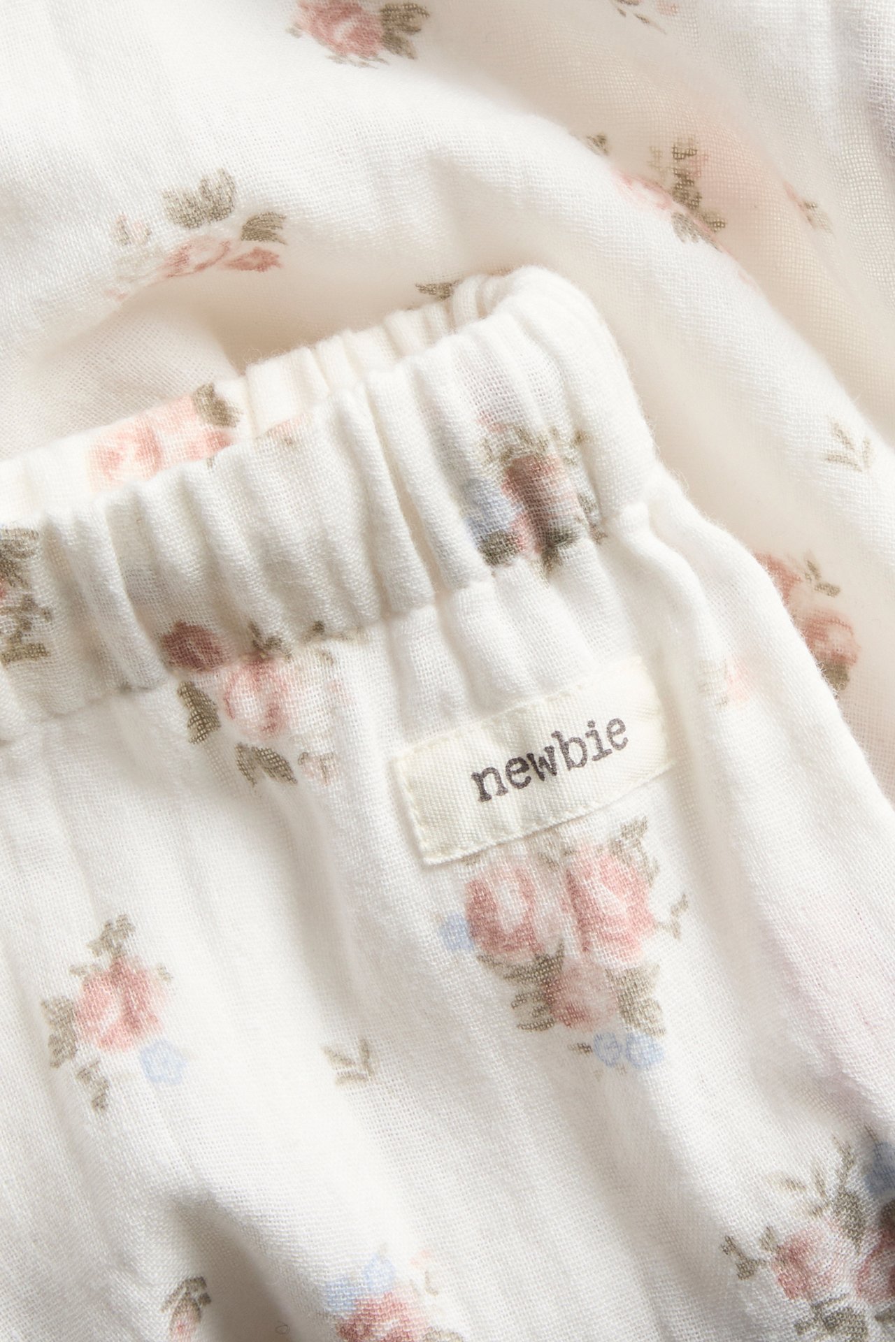 Nærbilde av offwhite tynne bomullsbukser med et delikat blomstermønster og elastisk linning.