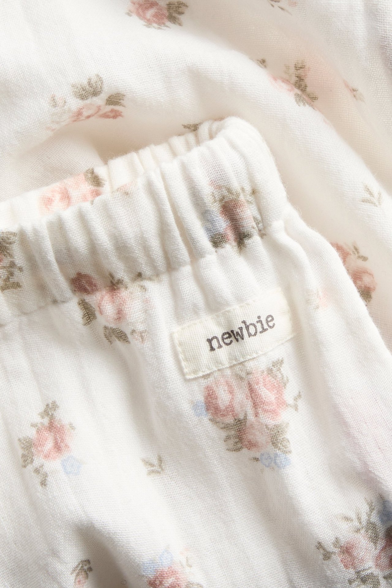 Närbild av benvita tunna bomullsbyxor med ett delikat blommönster och resår i midjan.