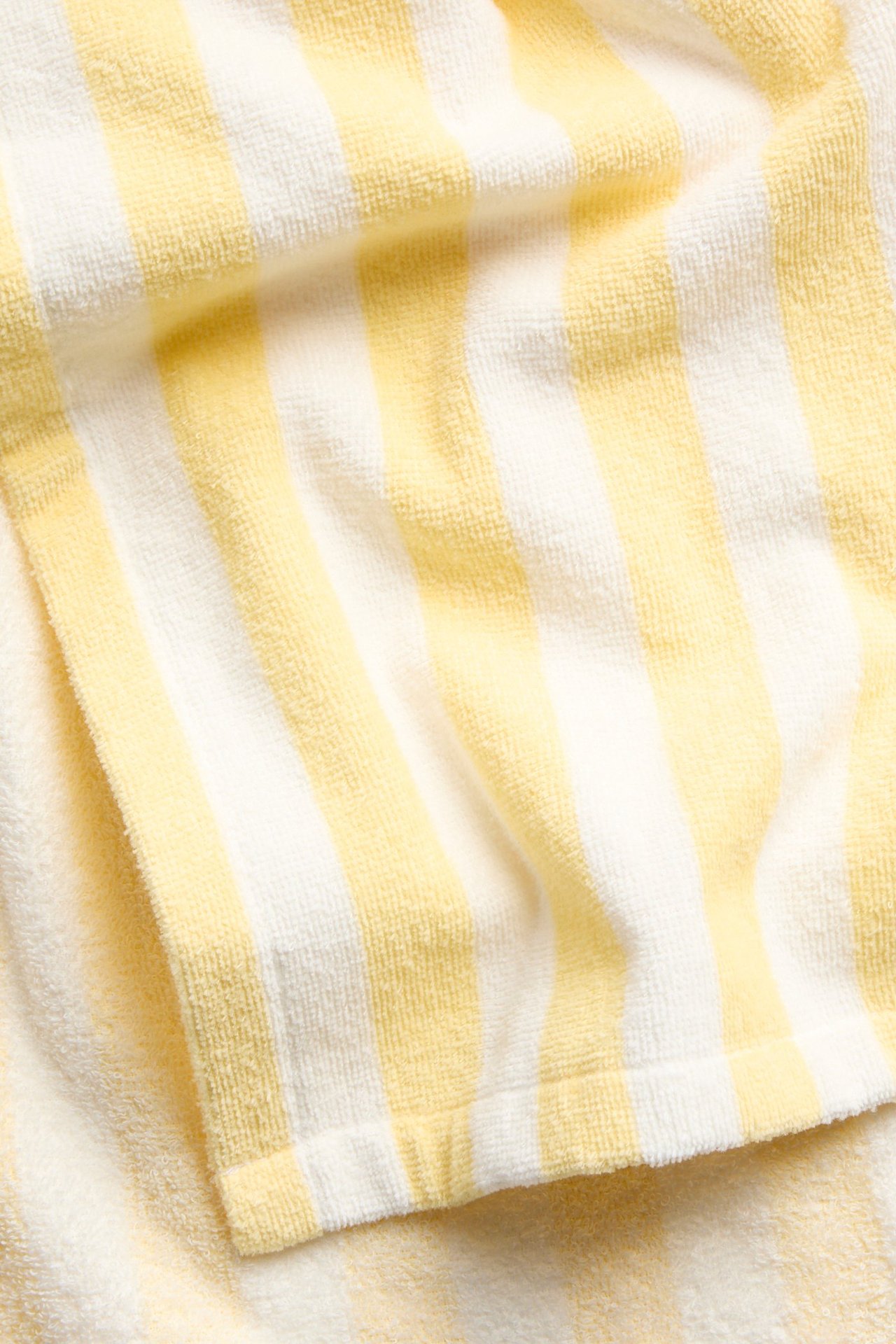 Zbliżenie na pasiastą, złamaną biel i jasnożółte bawełniane ponczo kąpielowe z frotte.