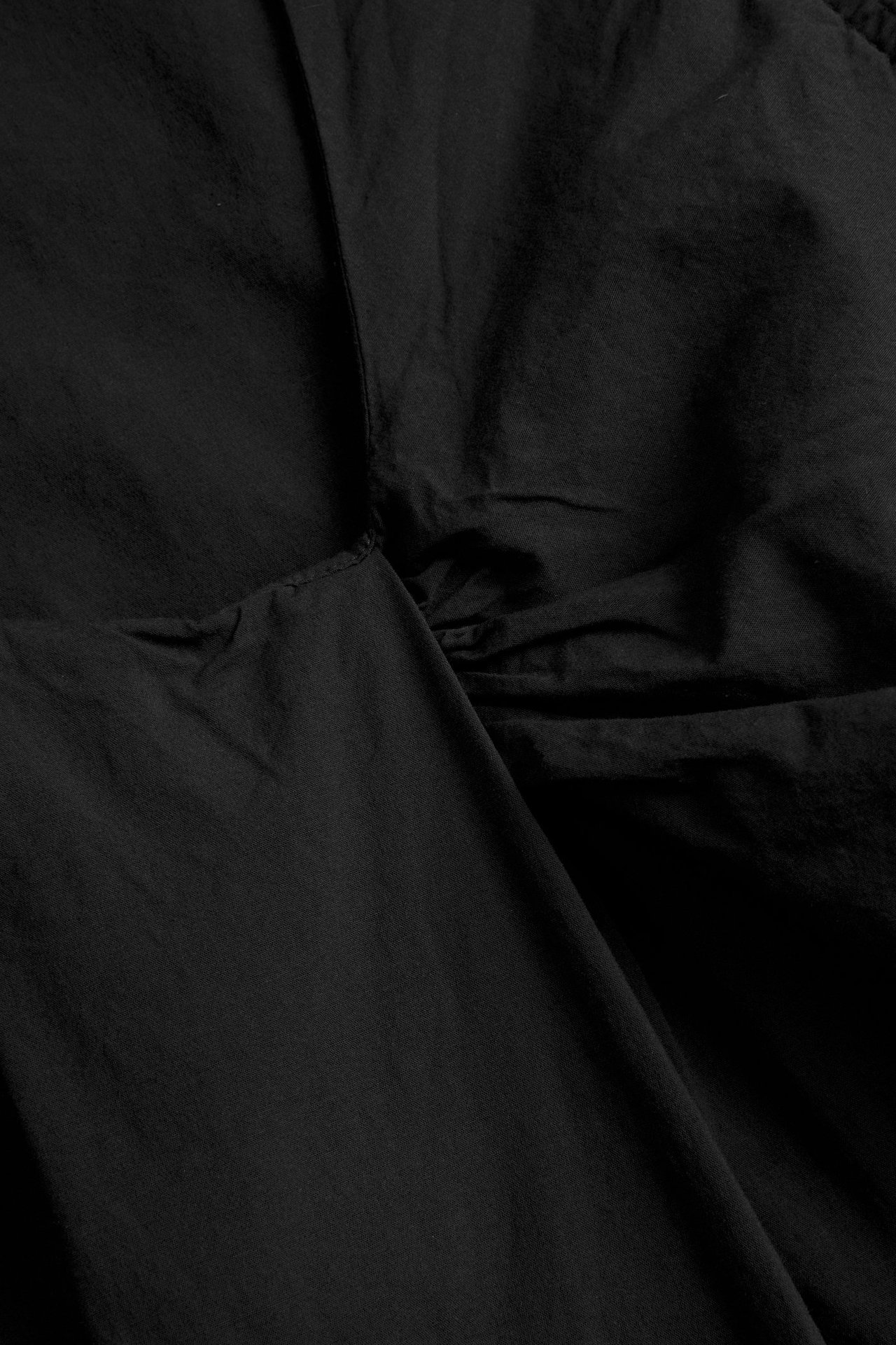 Zbliżenie czarnego topu z tkanej popeliny z zakładanym detalem, wykonanego z mieszanki bawełny i wiskozy.