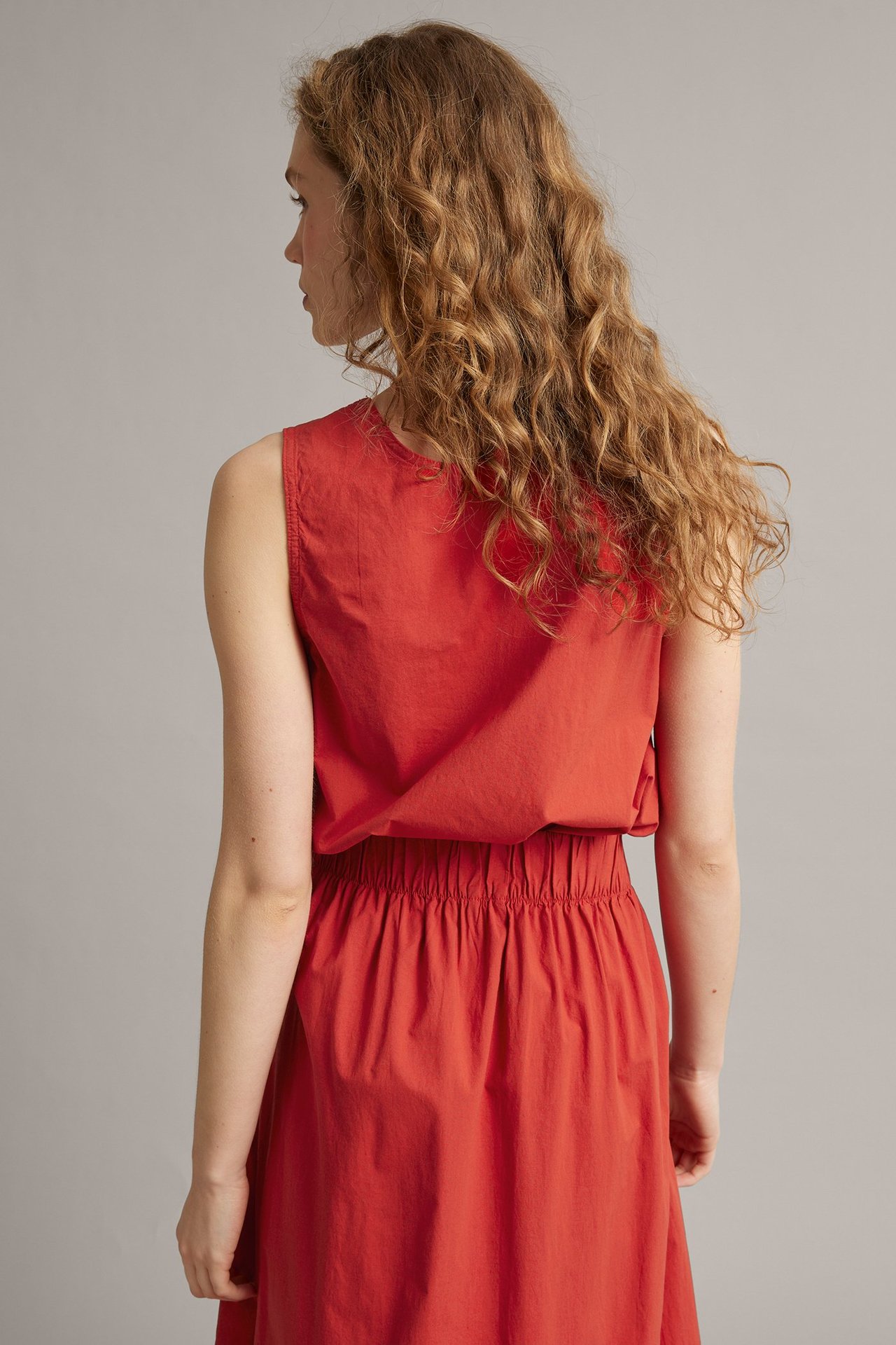 Ryggvy av en kvinna i en lös röd ärmlös topp i bomull-viskos och matchande röd kjol med resår i midjan.