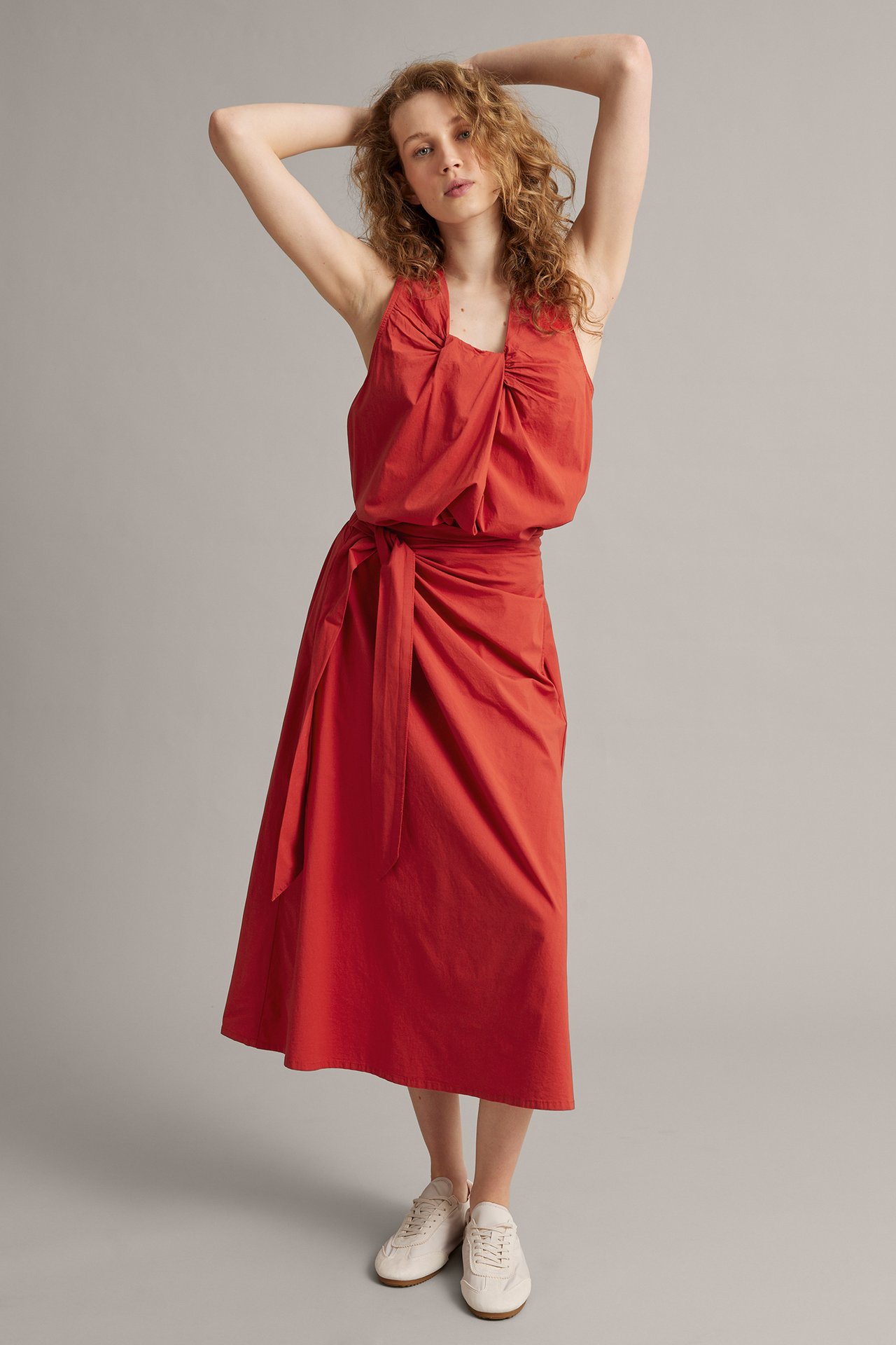 Framifrån: kvinna i röd rynkad poplinlinne, matchande röd omlottkjol och vita sneakers.