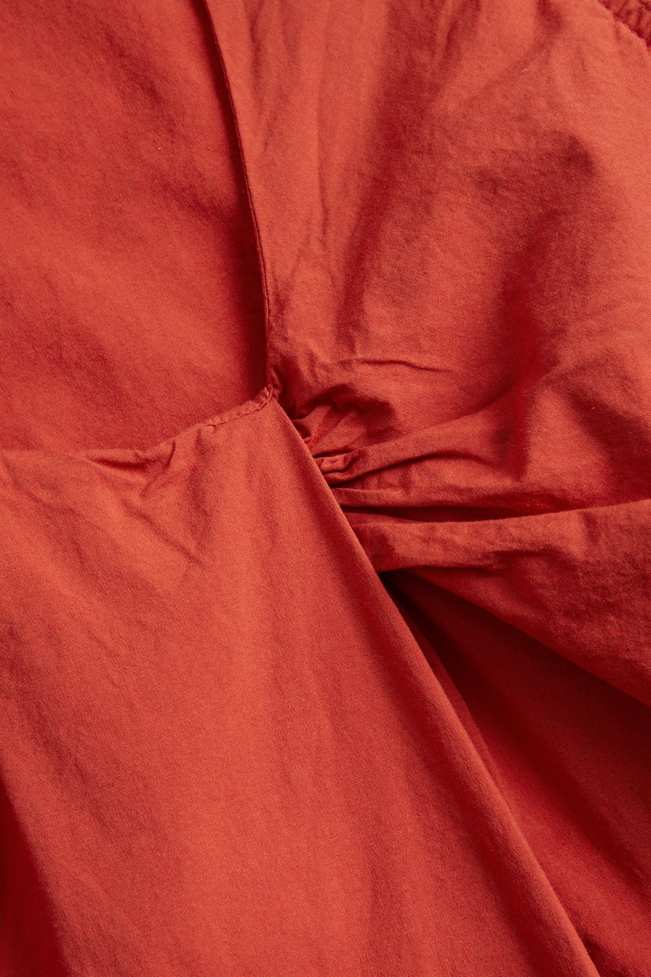 Zbliżenie na czerwony top z bawełny i wiskozy z dekoltem kopertowym.