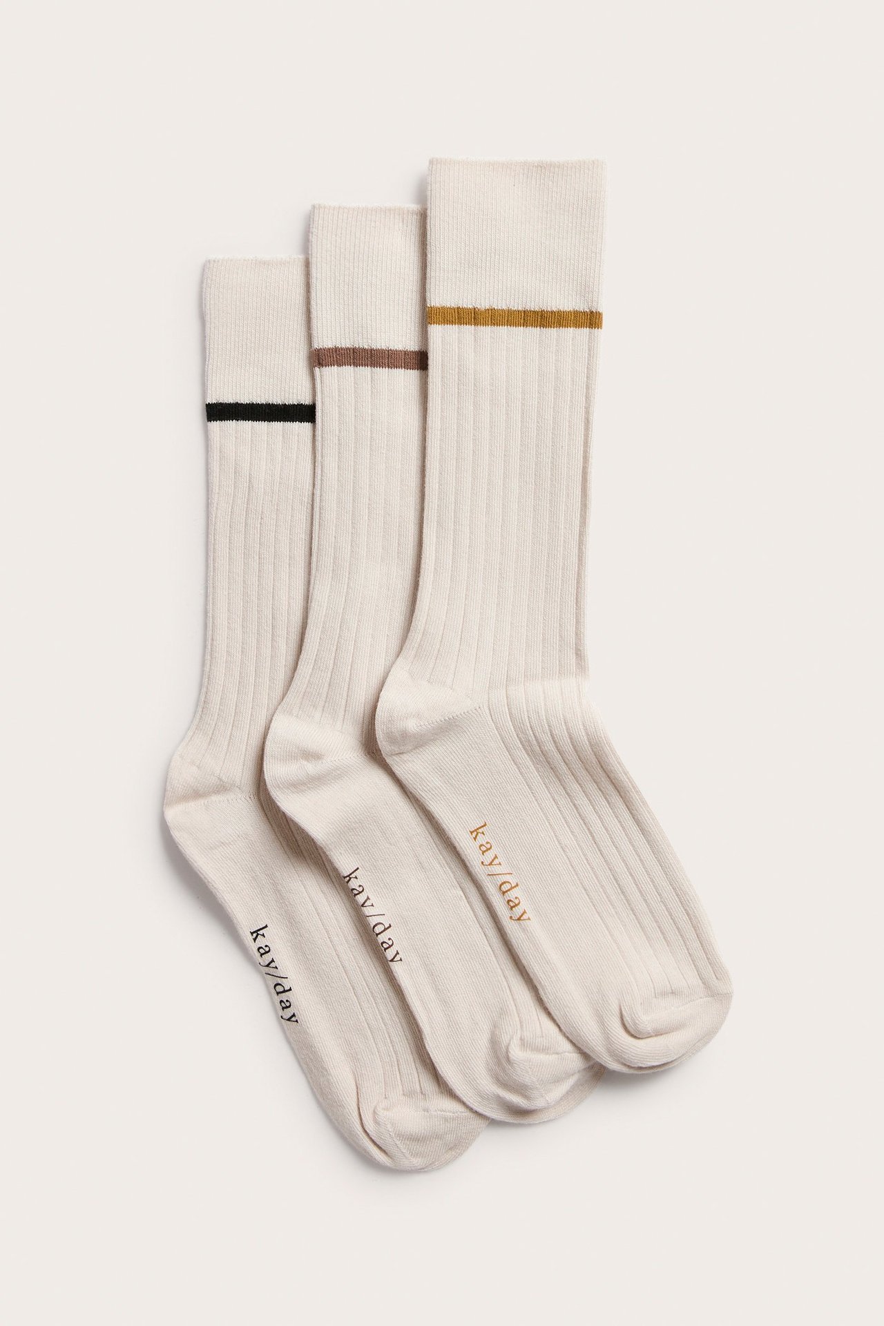 Widok z przodu na trzy jasnobeżowe, prążkowane skarpetki, każda z innym kolorowym paskiem przy brzegu.